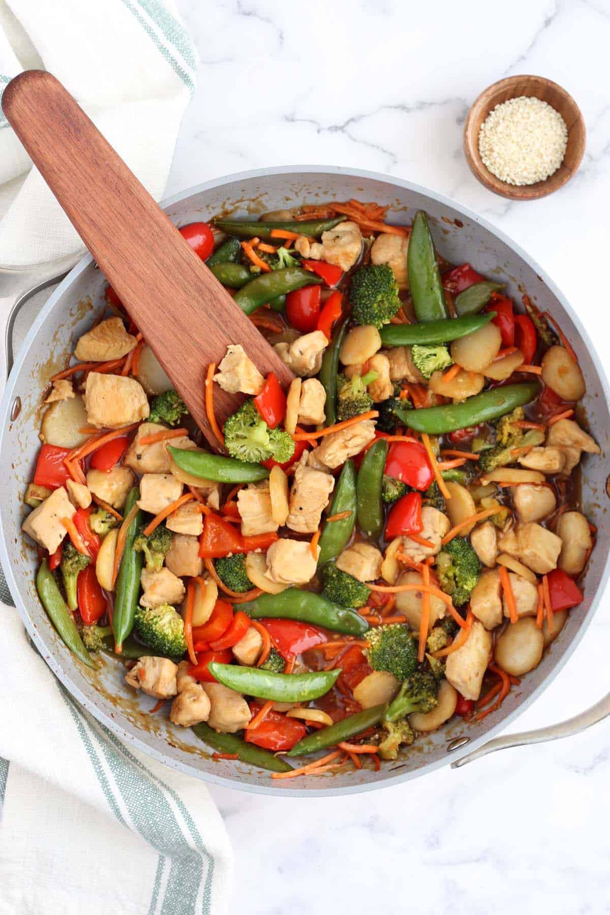 chicken stir fry in a large skillet with a wooden utensil