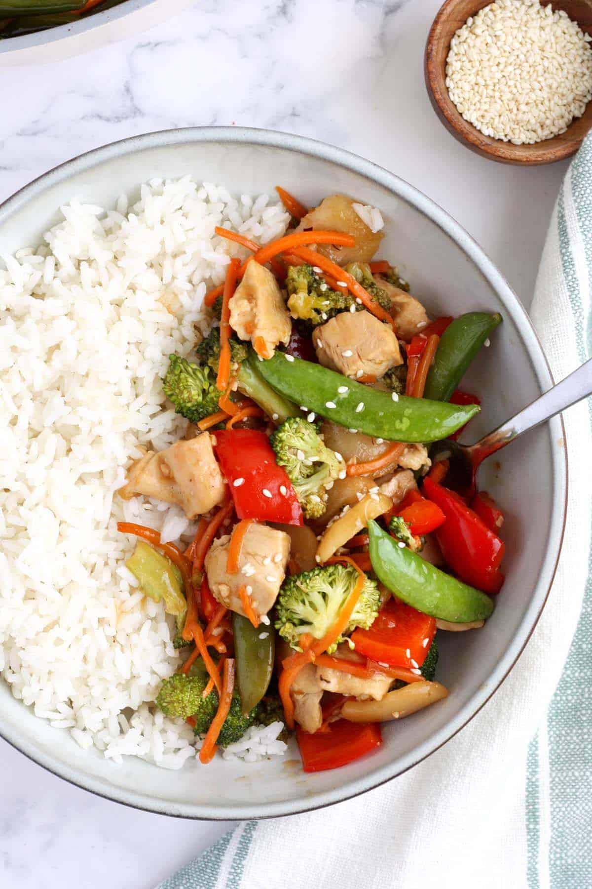 a bowl of white rice and stir fry chicken topped with sesame seeds