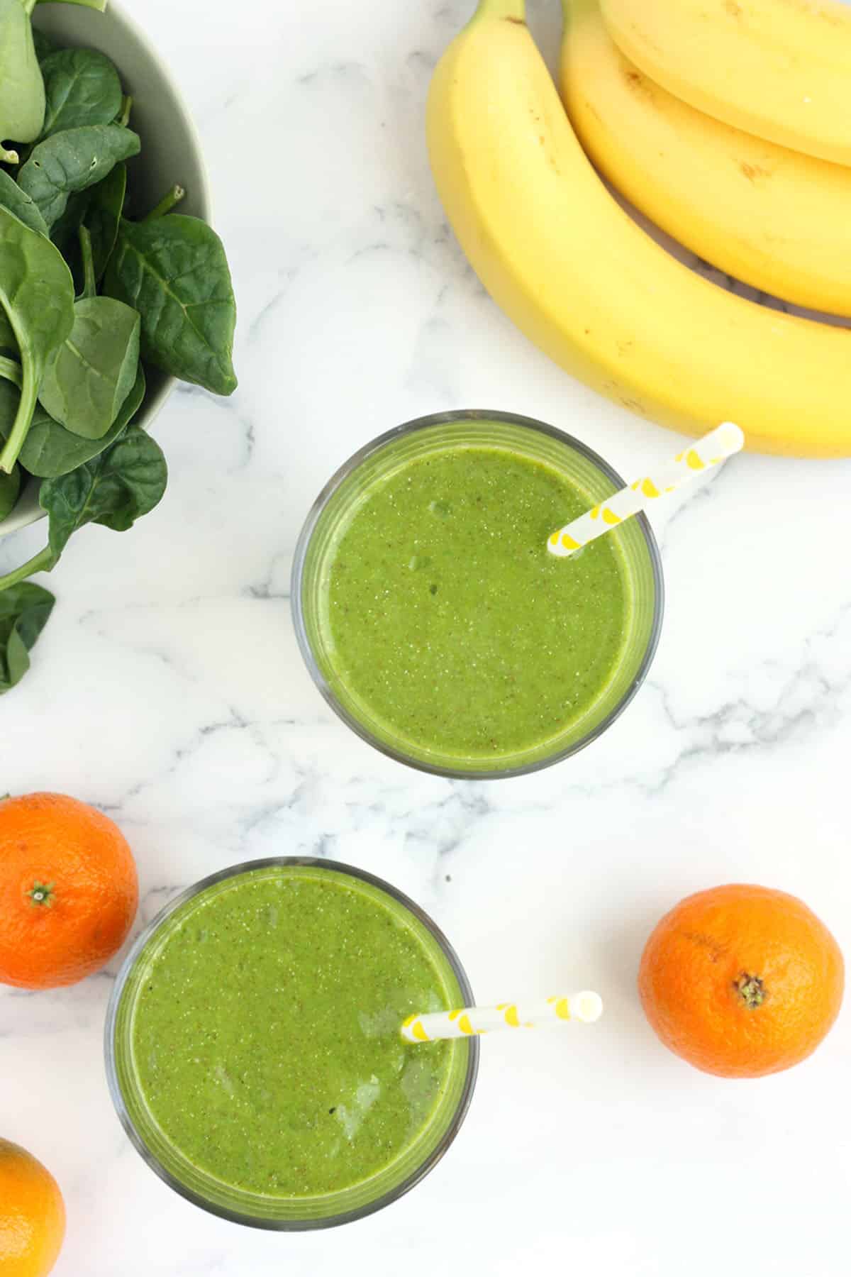 Overhead shot of green smoothie, bananas, spinach and oranges