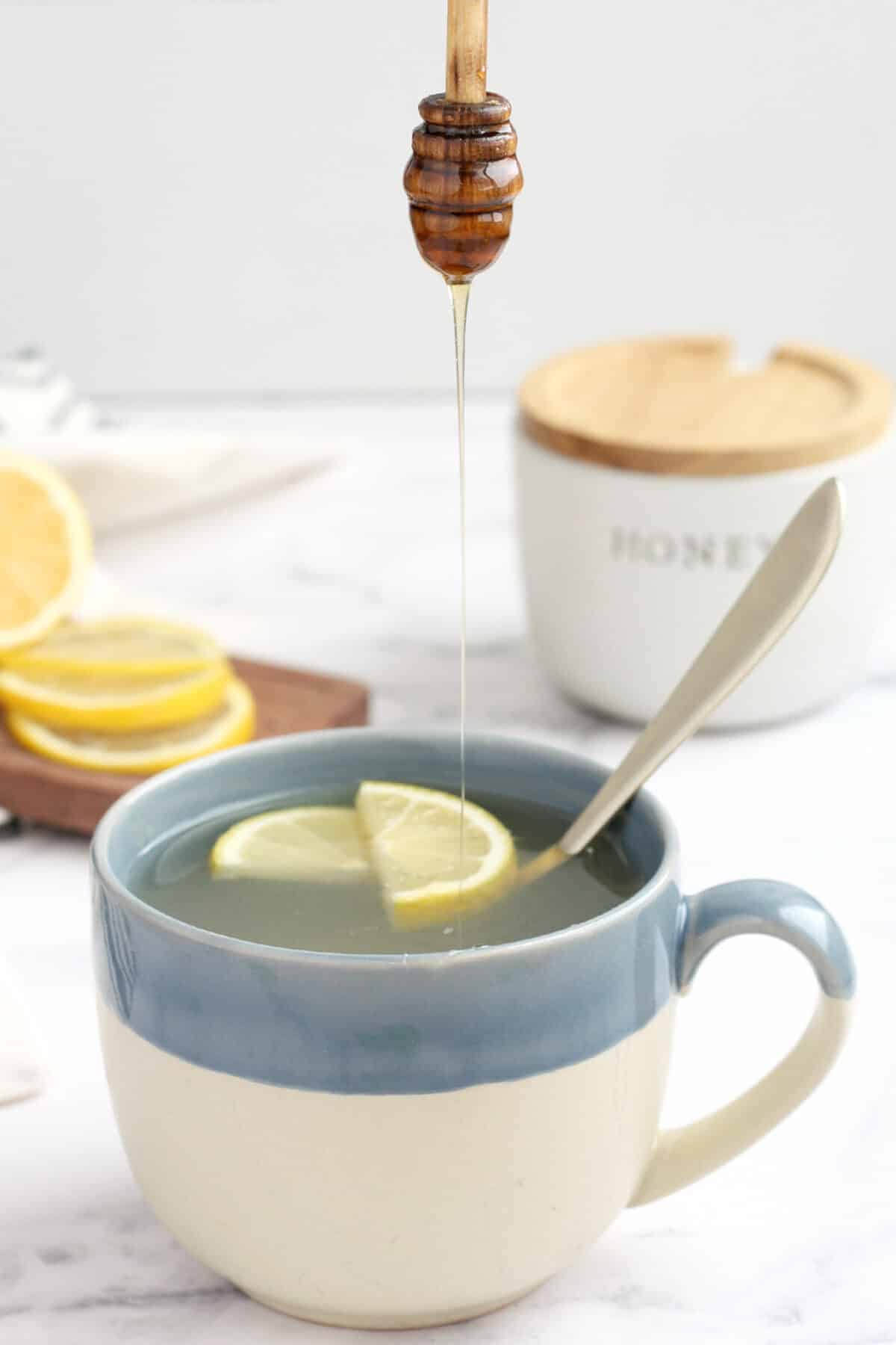 A mug of honey lemon tea with a slice of lemon and a drizzle of honey