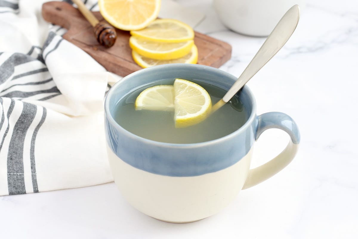 a mug of honey lemon tea with a kitchen linen and lemon slices