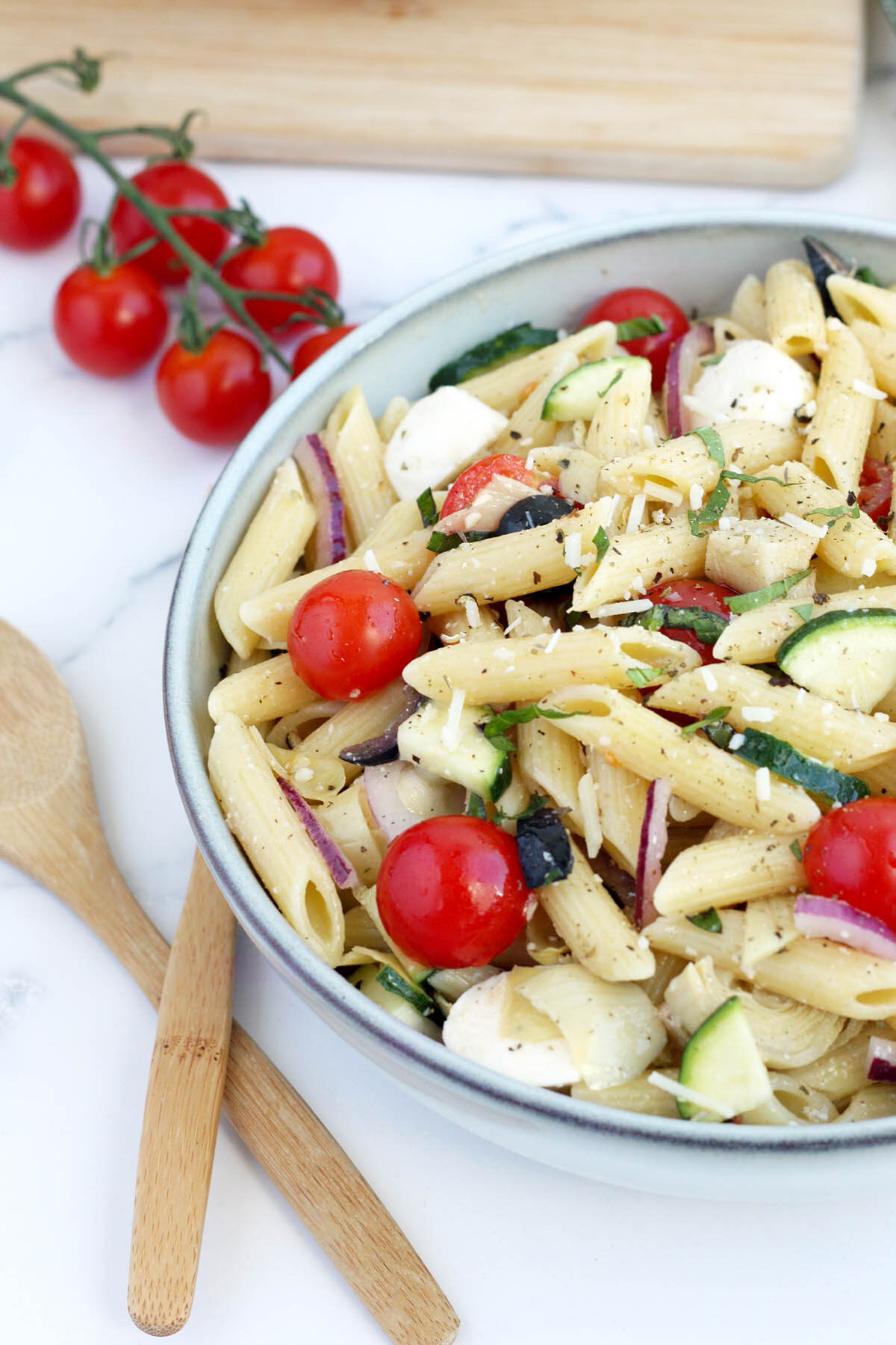 italian pasta salad with tomatoes and zucchini in a serving bowl with wooden utensils