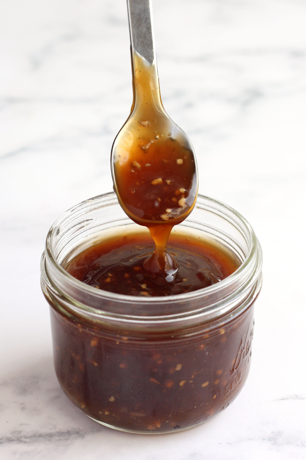 a spoonful of stir fry sauce dripping into a glass jar