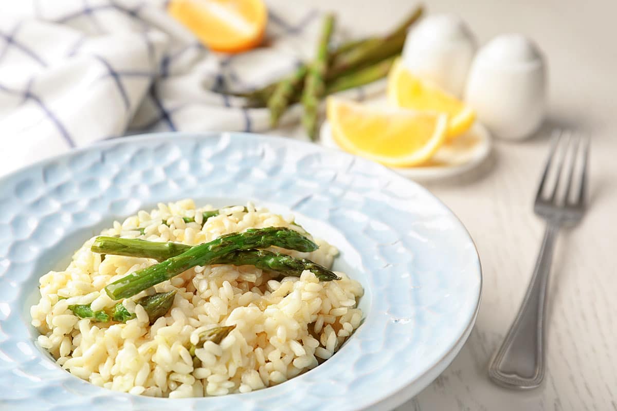 Delicious risotto with asparagus on white wooden table, closeup