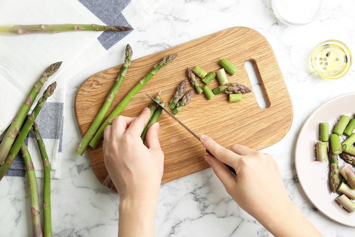 Woman cutting asparagus at white marble table, top view