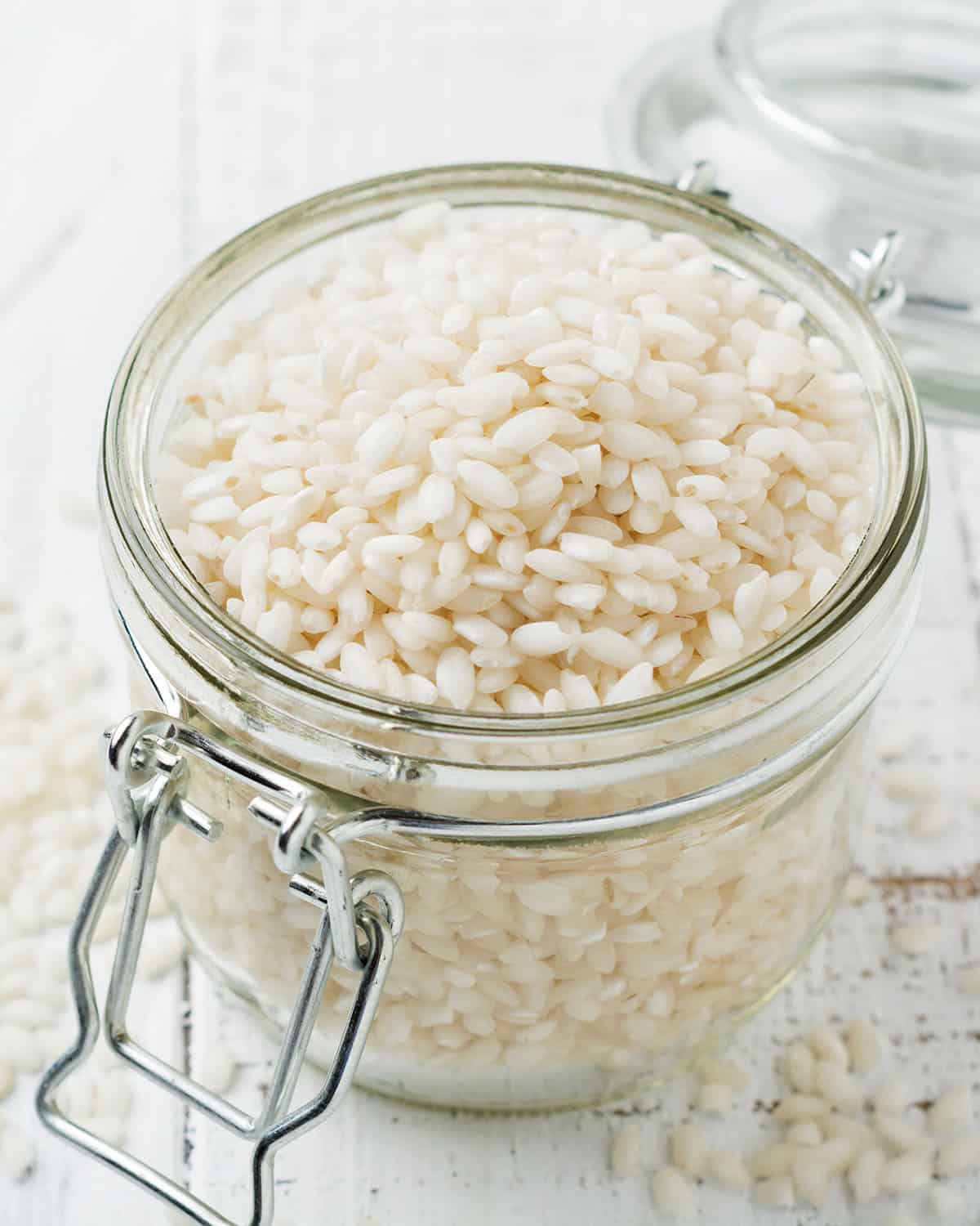 Raw White rice variety Arborio for Italian risotto dishes in glass jar on  white concrete or stone background. Selective focus. Copy space.