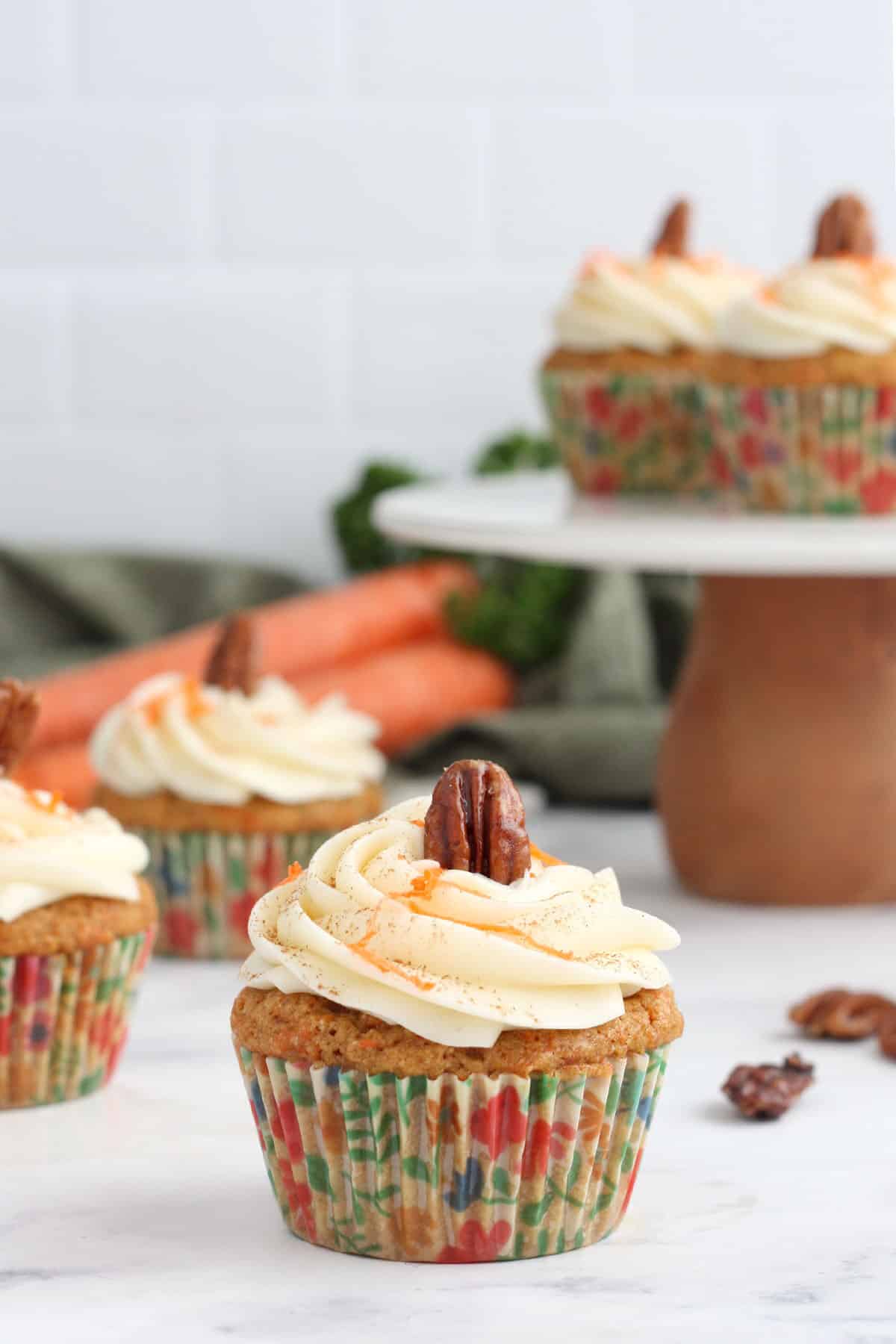 carrot cake cupcake topped with cream cheese frosting and a glazed pecan