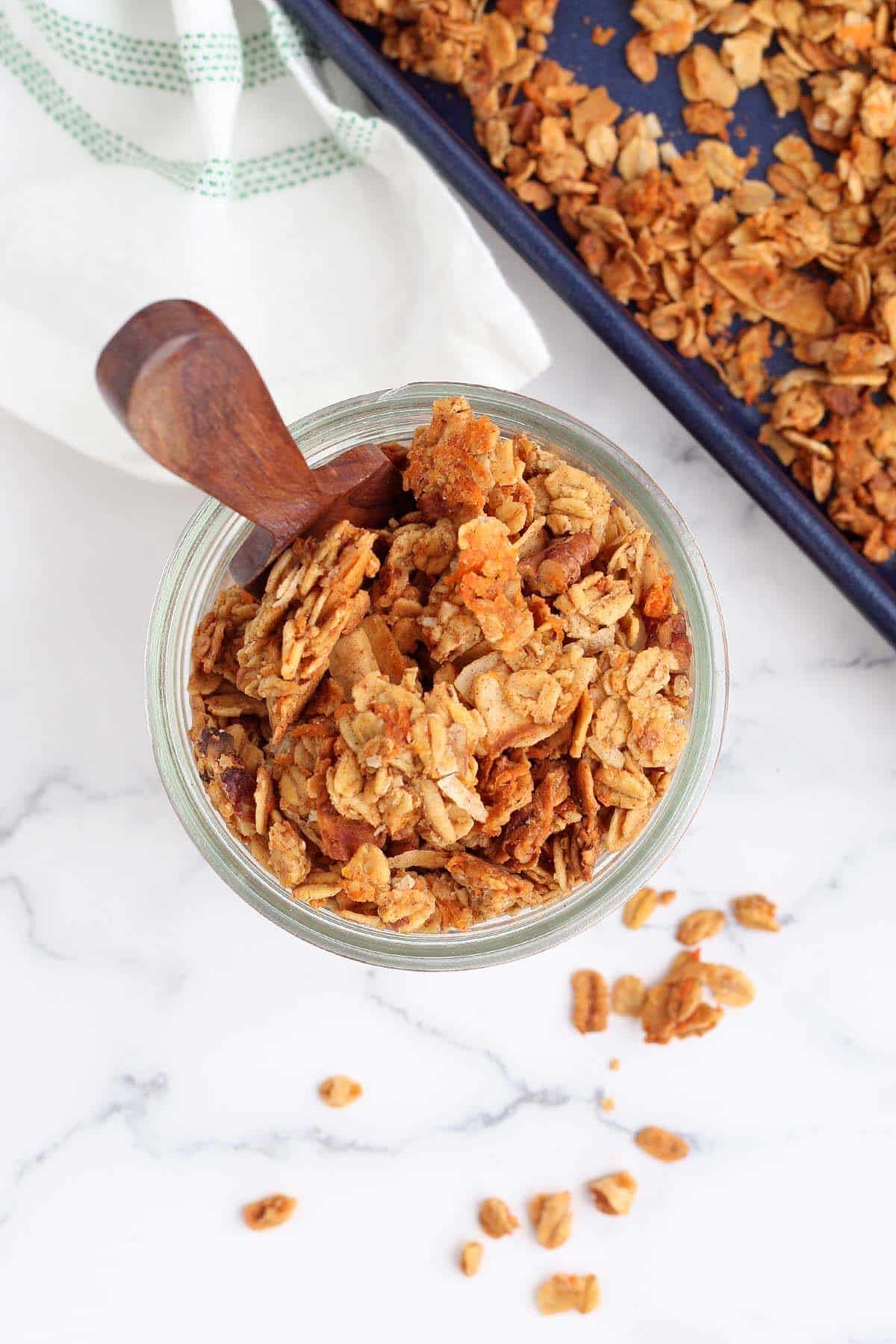 An overhead shot of carrot cake granola in a mason jar with a wooden ladle