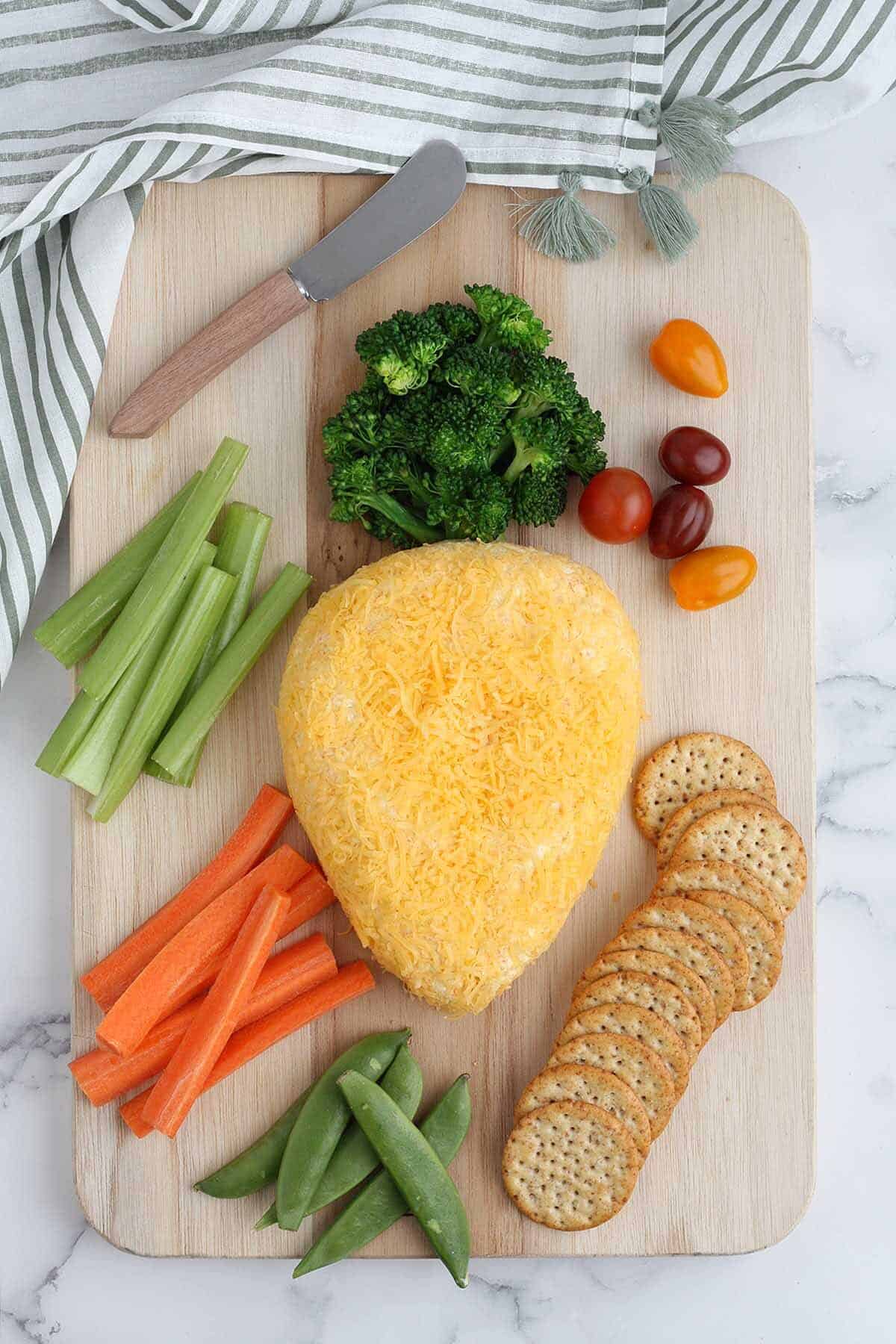 an overhead shot of a cheese ball with broccoli as the carrot top and served with assorted vegetables and crackers