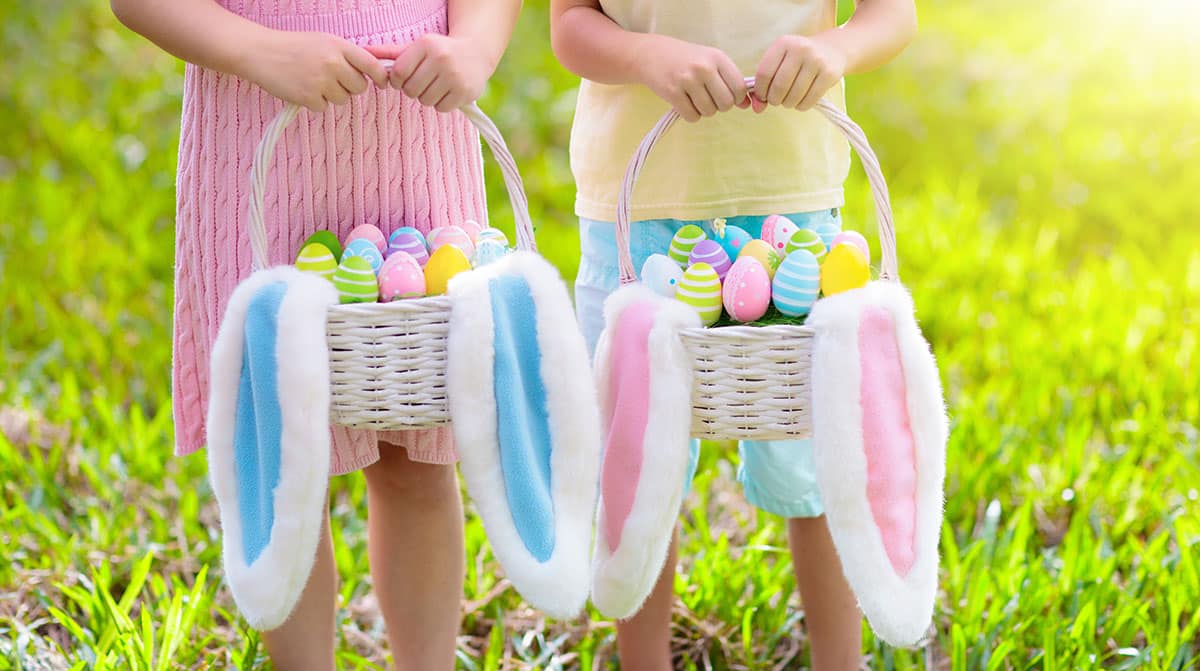 Kids with eggs basket and bunny ears on Easter egg hunt in sunny spring garden. Little boy and girl searching for colorful candy and chocolate eggs with rabbit basket. Children celebrating Easter.