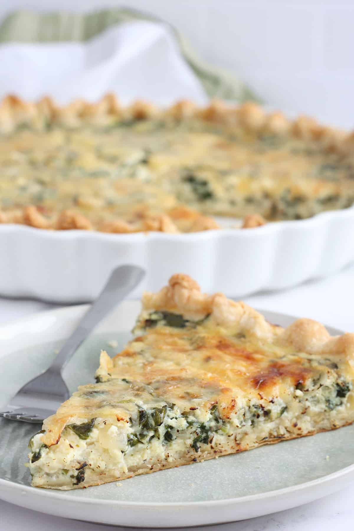 Slice of spinach quiche on serving plate with fork