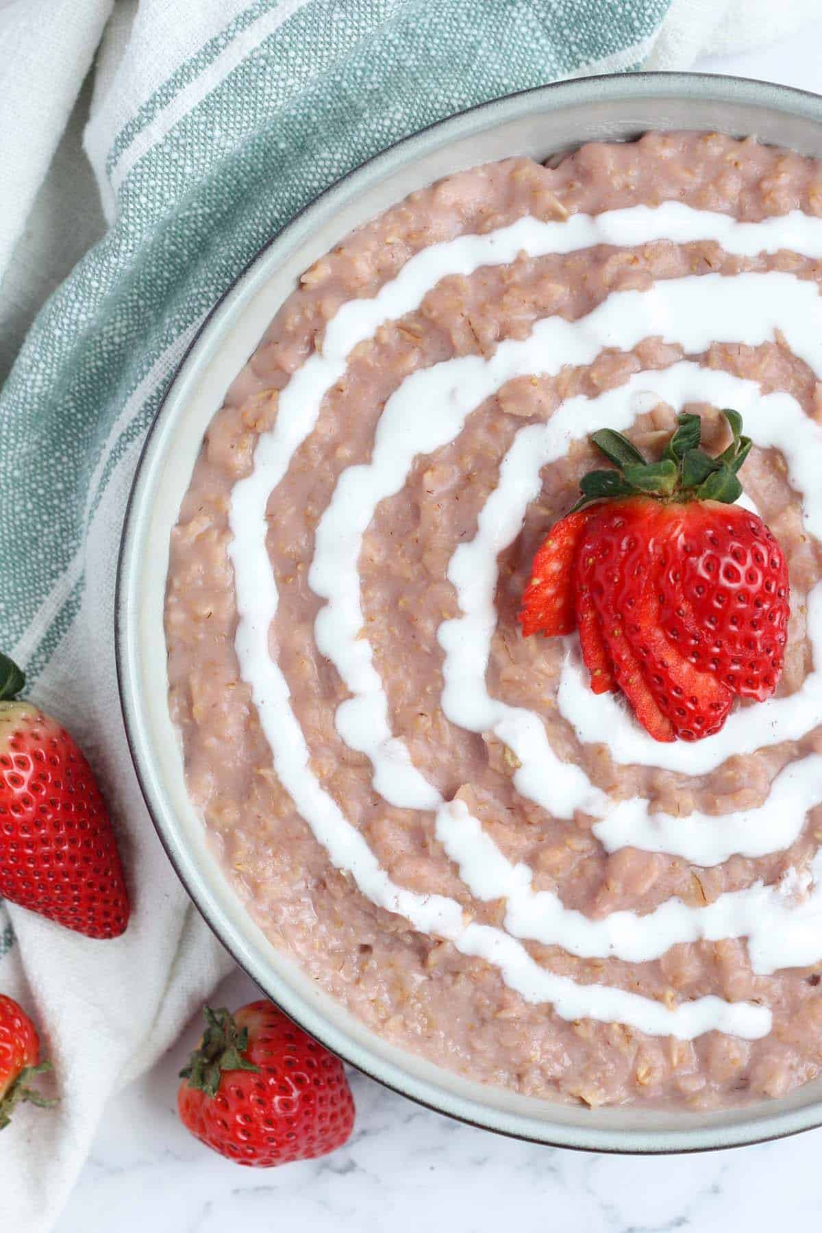 a close up picture of strawberry oatmeal topped with a cream swirl