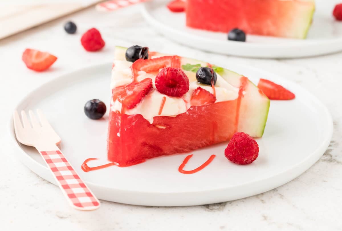 A slice of watermelon fruit pizza on a white serving plate, topped with fresh raspberries, blueberries, and strawberries.