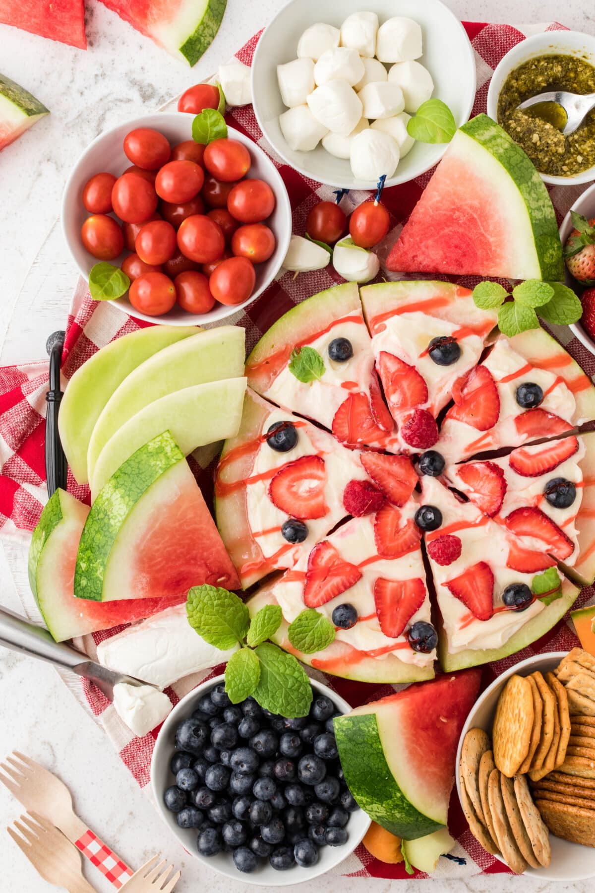 A summer charcuterie board with a fruit pizza and bowls of fresh berries and tomatoes.