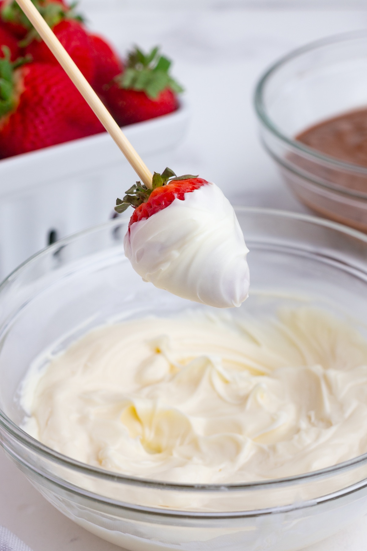 a strawberry on a wooden skewer dipped in melted white chocolate