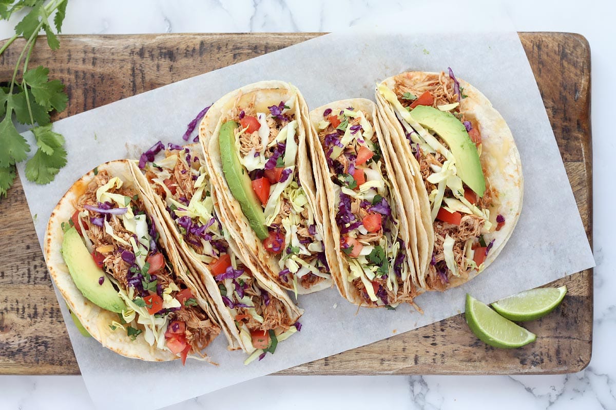 chicken tacos lined up on a wooden serving board with fresh cilantro and lime