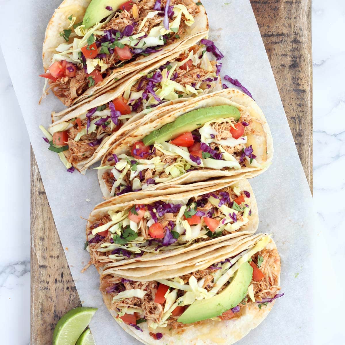 crockpot chicken tacos in flour tortillas topped with tomatoes and avocado slices