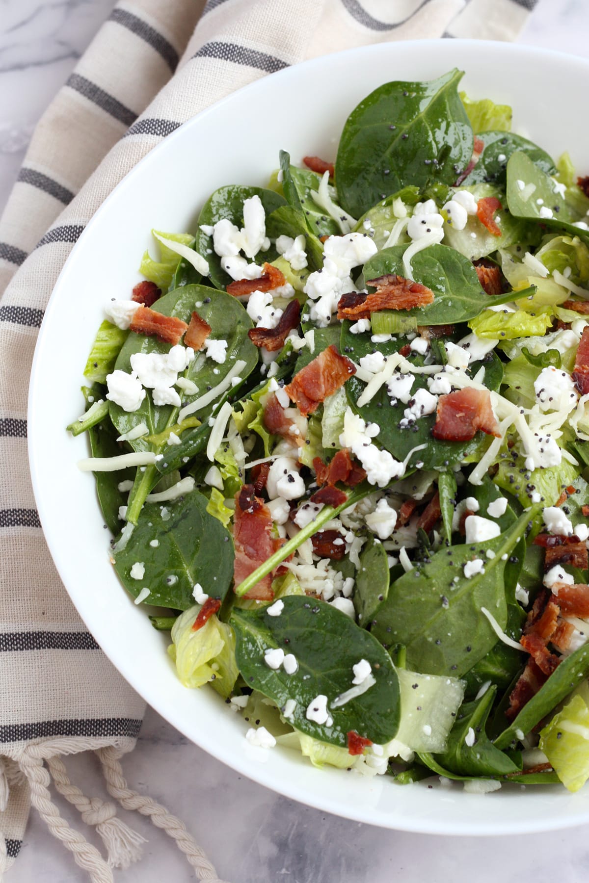 Spinach salad with cheese and bacon in a white serving bowl.