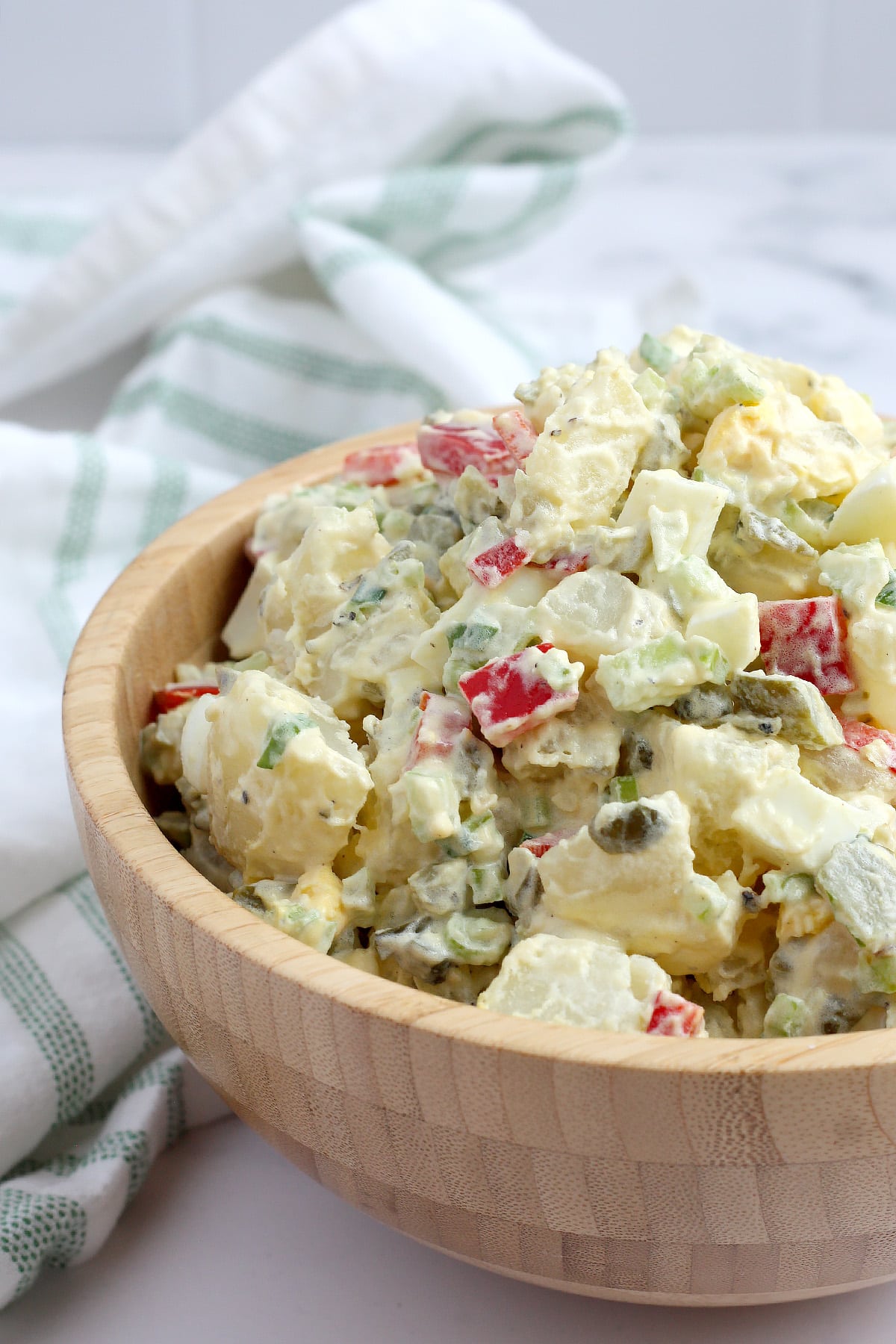 A wooden serving bowl full of potato salad with pickles and red peppers.