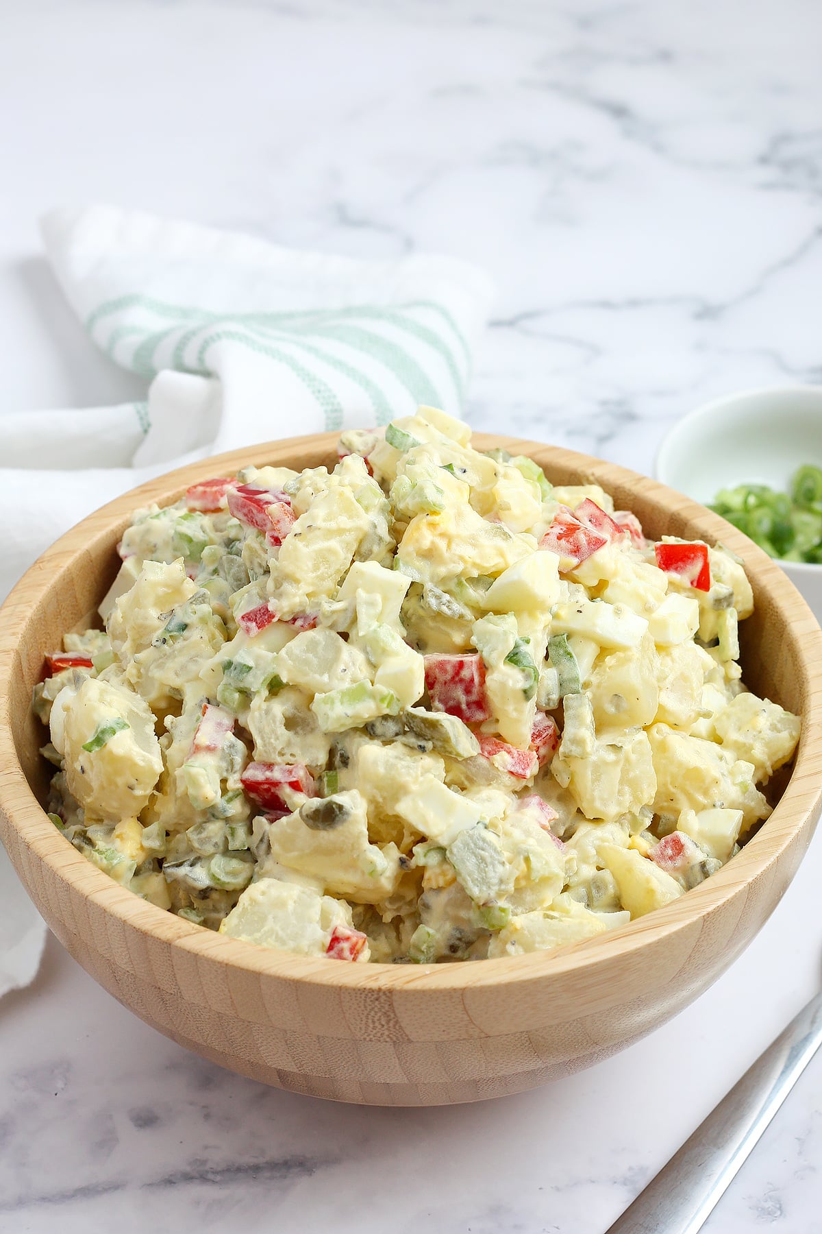 A wooden bowl topped with potato salad in a light dressing.