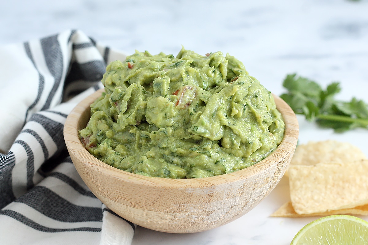 fresh guacamole in a wooden serving bowl with fresh limes and cilantro