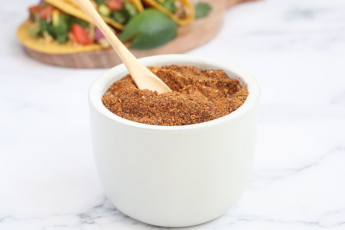 a ceramic bowl and wooden spoon filled with homemade taco seasoning