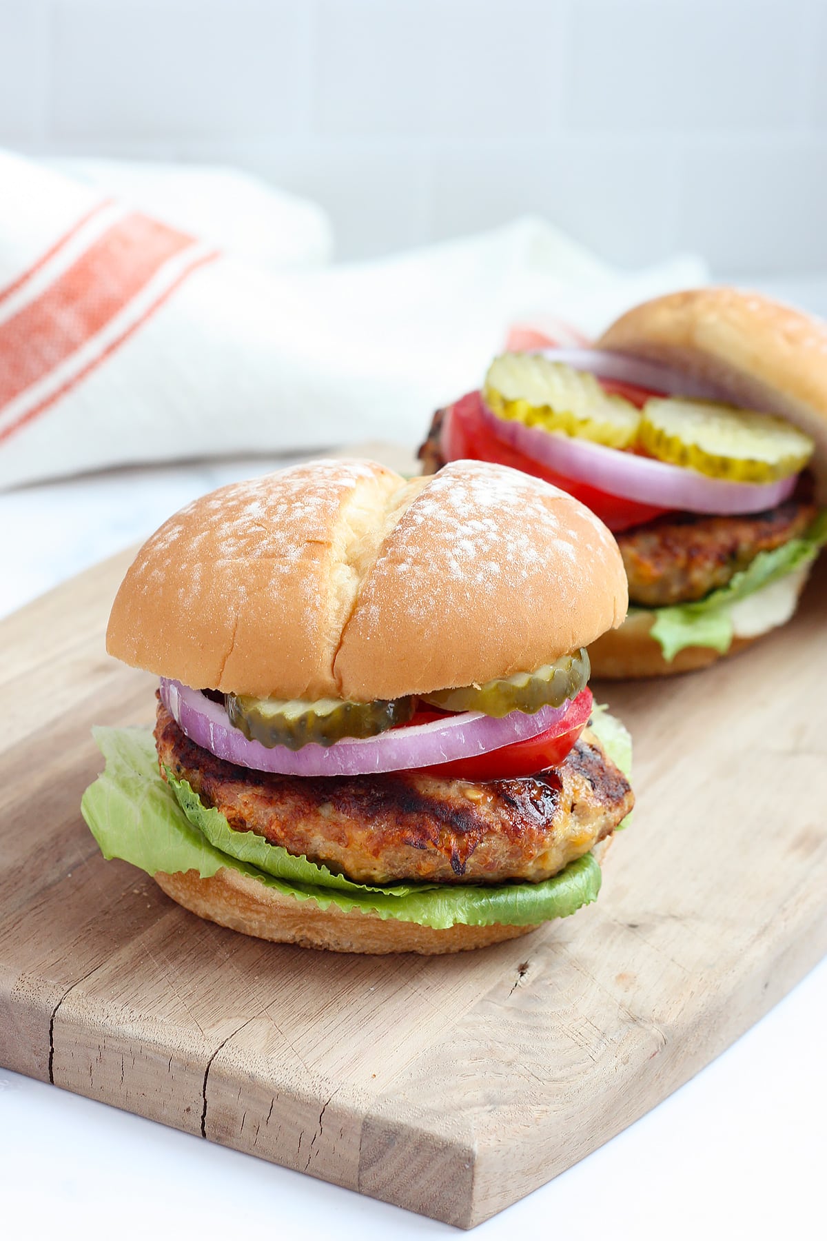 Juicy turkey burgers with lettuce, tomatoes and onions on a wooden cutting board.