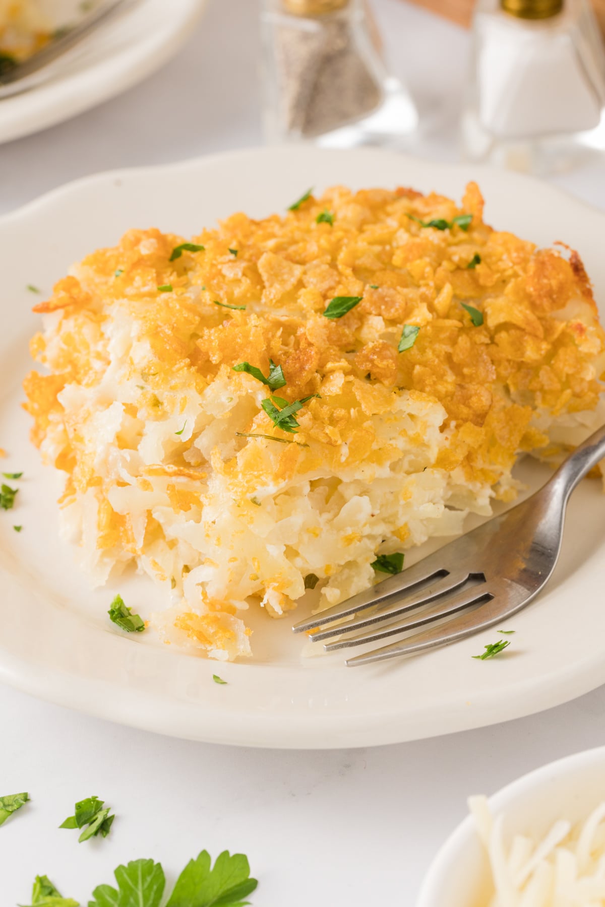 A large serving of cheesy potatoes topped with fresh parsley on a white serving plate with a fork.