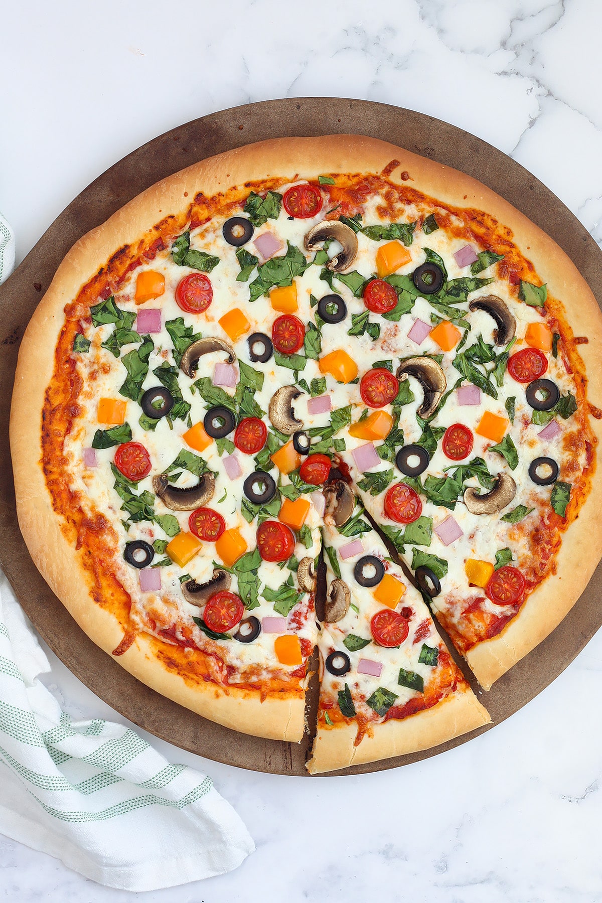 A homemade veggie pizza with one slice cut out on a round pizza stone.