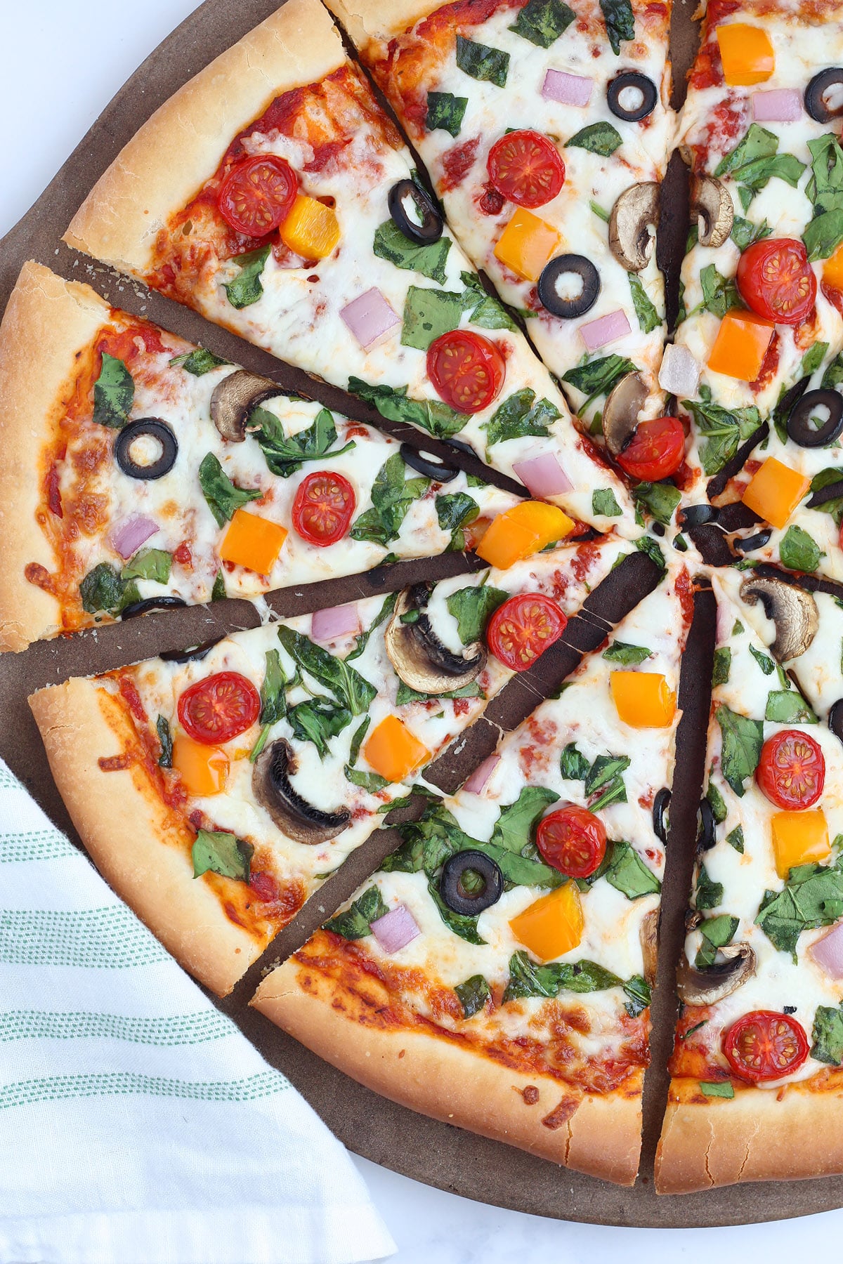 A homemade pizza topped with fresh veggies on a pizza stone.