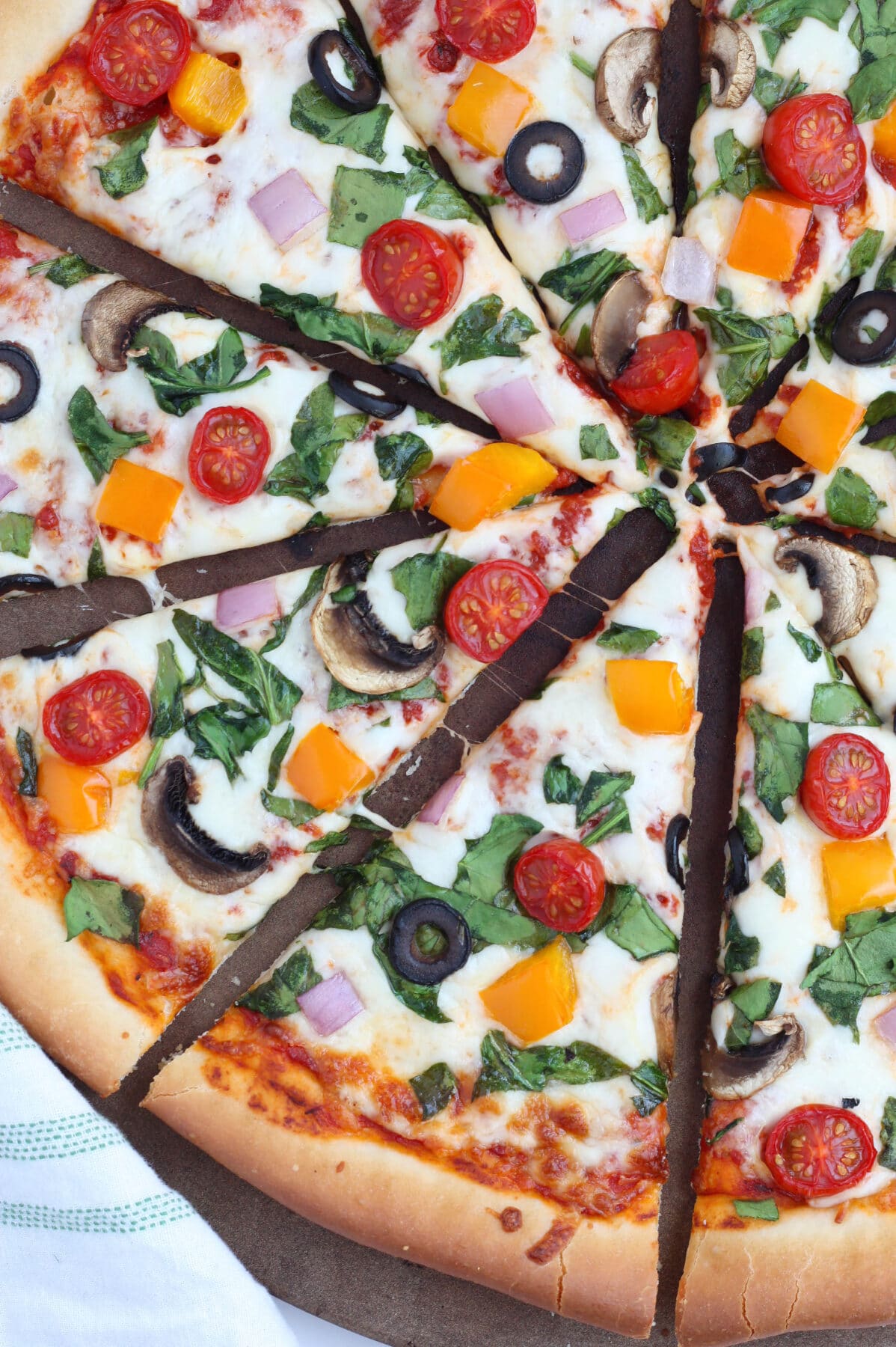 A close up shot of homemade pizza topped with fresh tomatoes, spinach, onions and bell peppers.