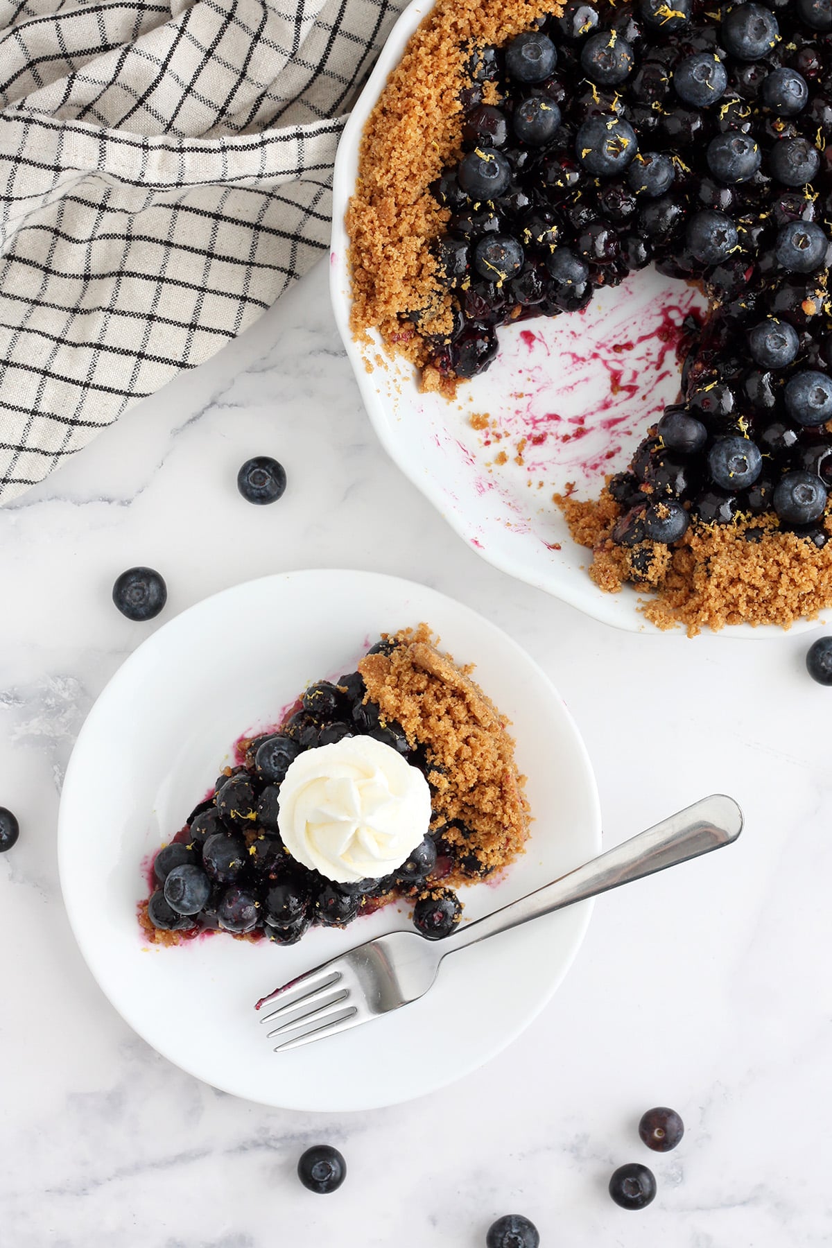 An overhead shot of a slice of no-bake blueberry pie with graham cracker crust on a white serving plate with a fork.