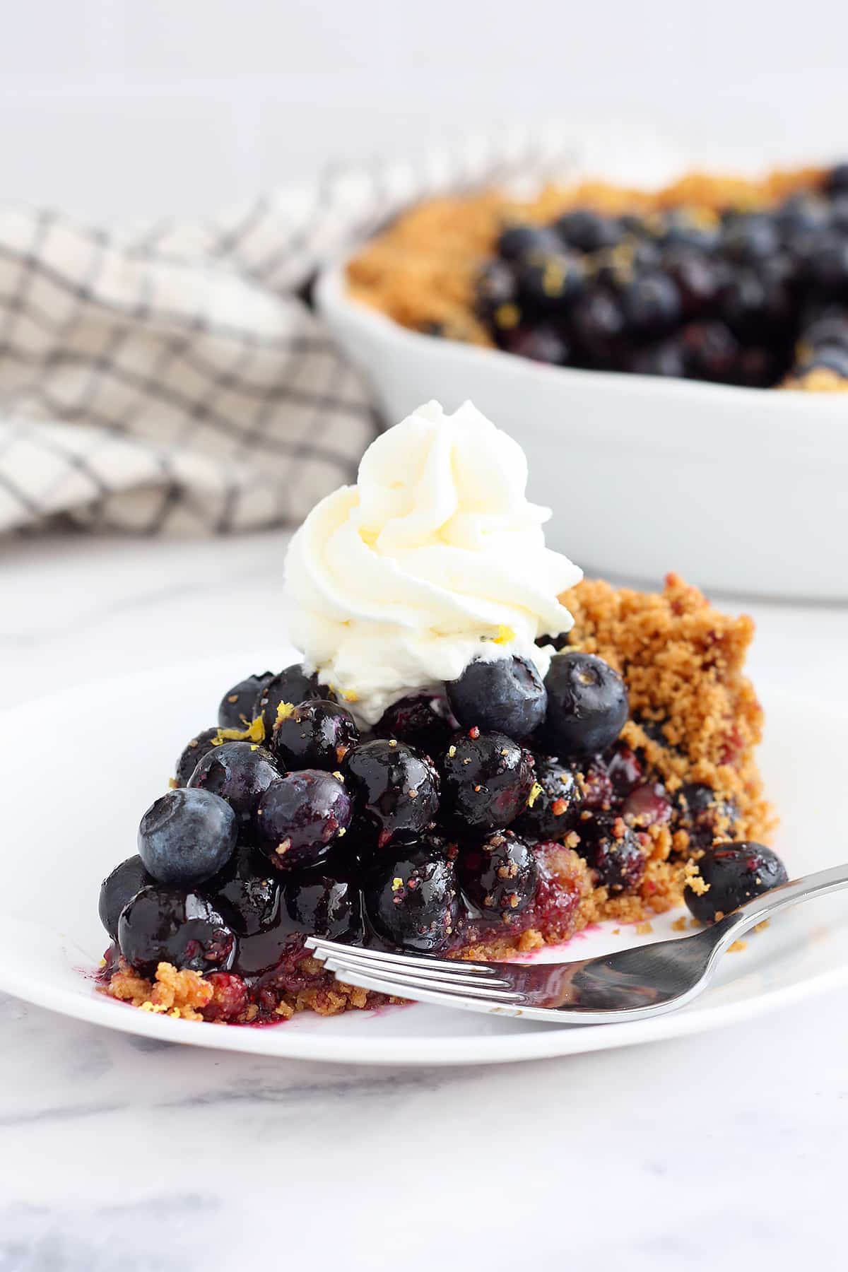A slice of no-bake blueberry pie on a white serving plate topped with a swirl of whipped cream.