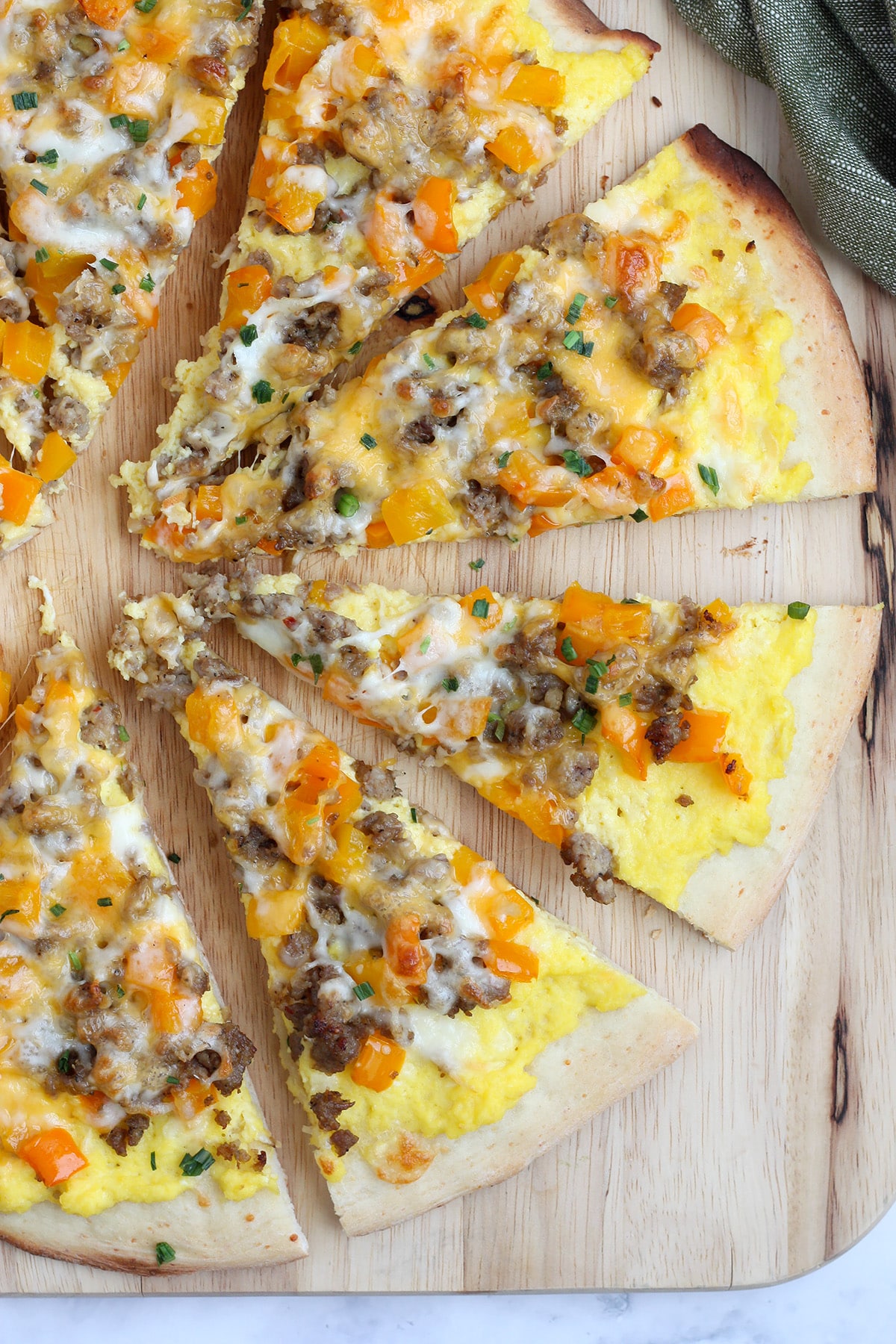 Breakfast Pizza topped with sausage and eggs on a wooden cutting board.