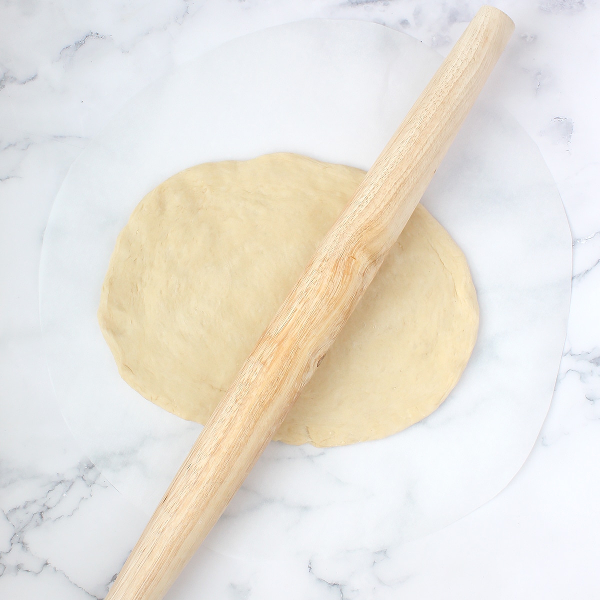 Homemade pizza dough rolled out into a thin circle with a french rolling pin.