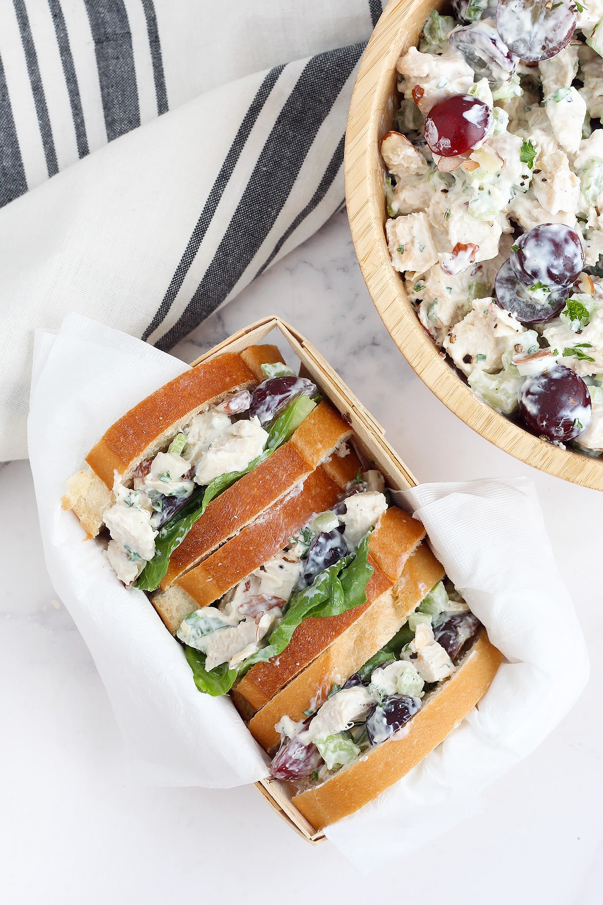 Chicken salad sandwiches on white bread with lettuce in a small basket with a white napkin.