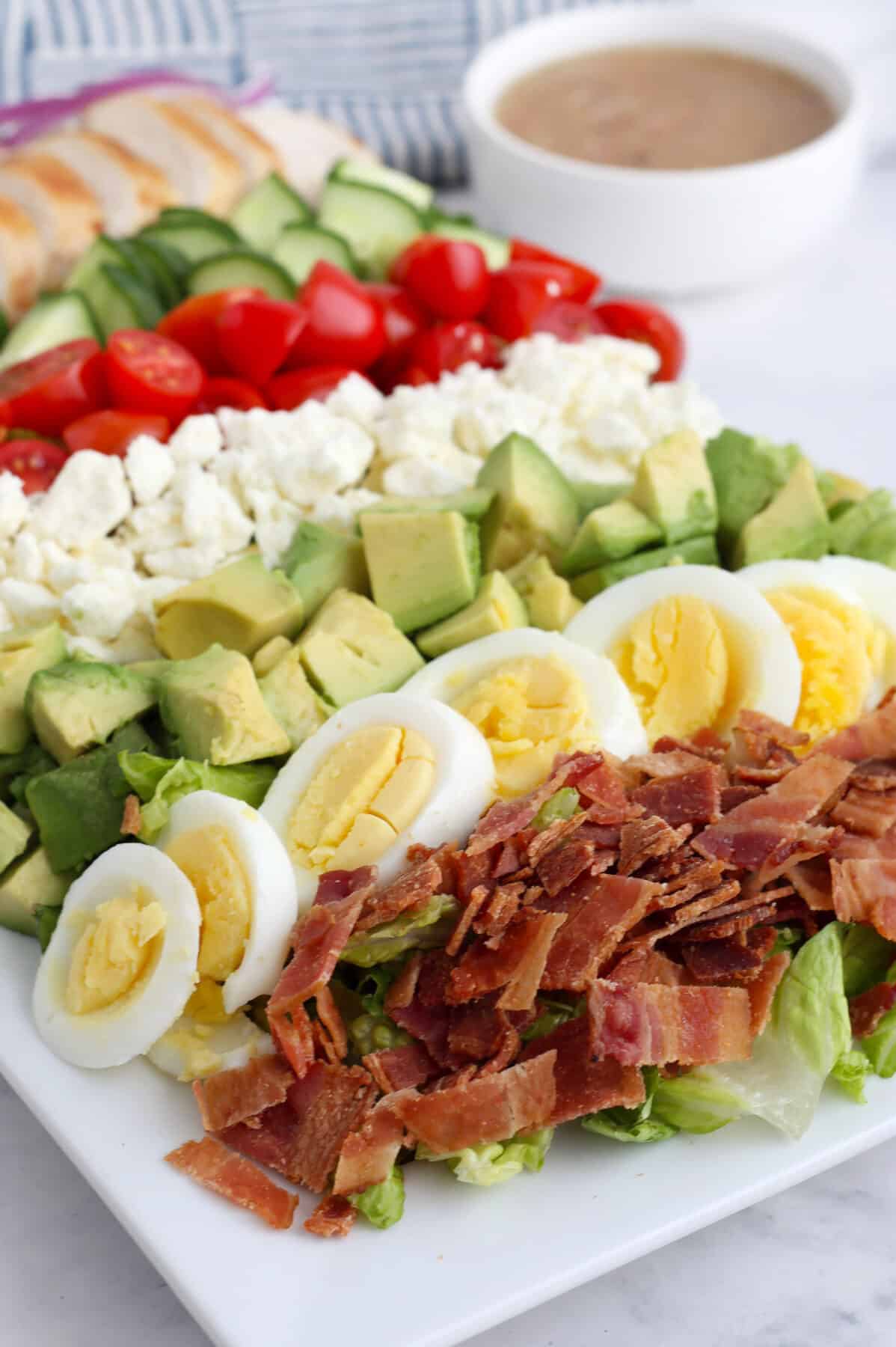 A close up image of our cobb salad recipe with a bowl of dressing.