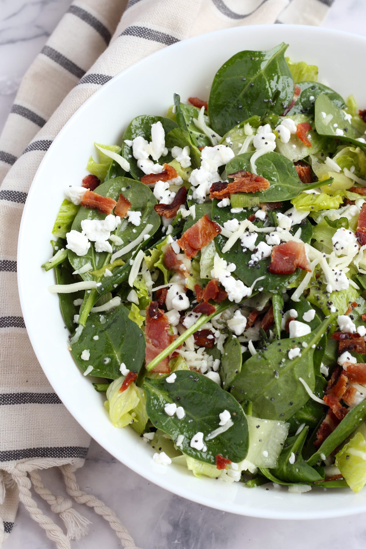 A bowl of spinach salad topped with bacon and cottage cheese.