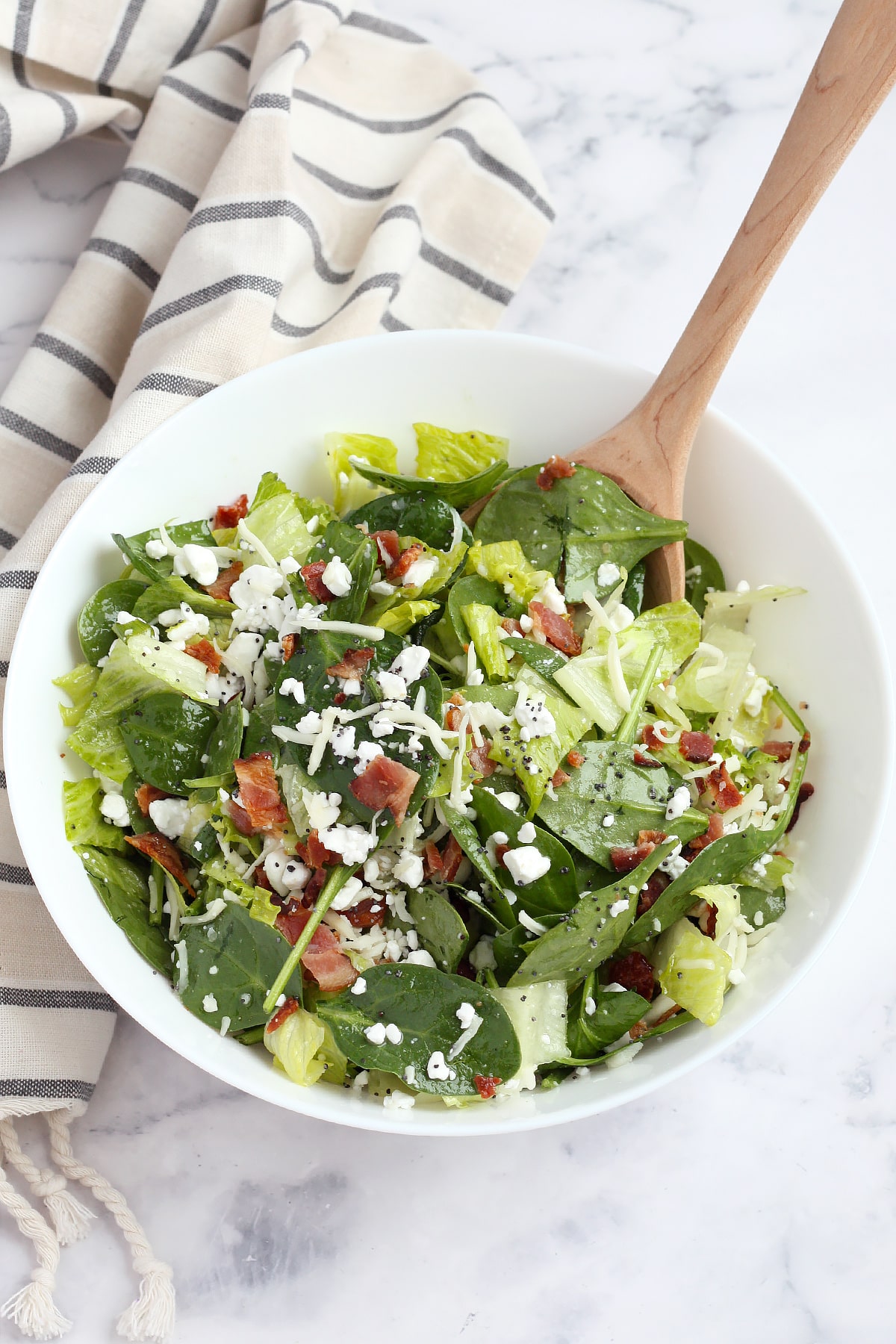 A large serving bowl filled with spinach and romaine salad with a wooden spoon.