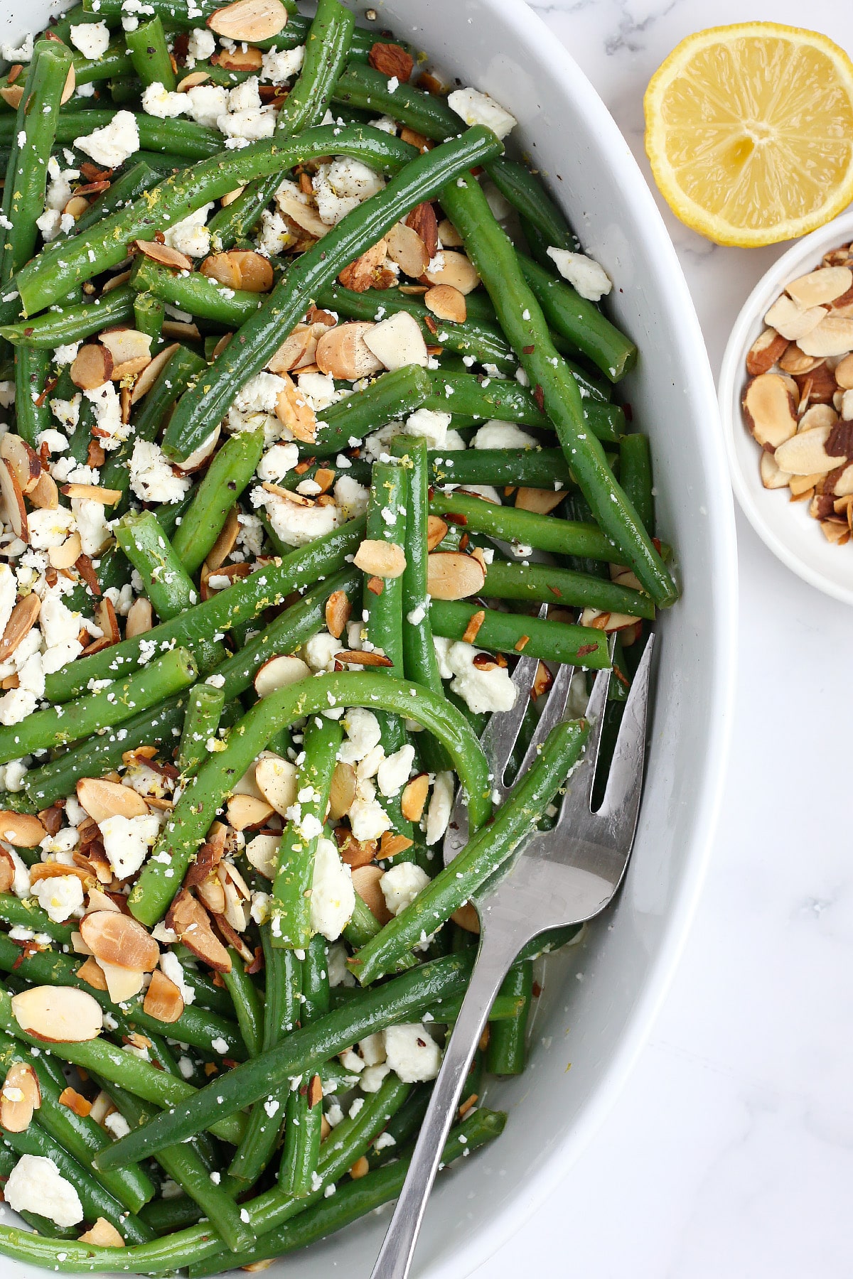 Fresh green beans topped with feta and almonds in a white serving dish.