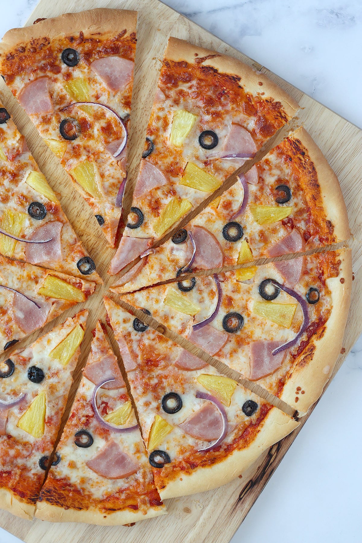 A sliced Hawaiian Pizza on a wooden cutting board.