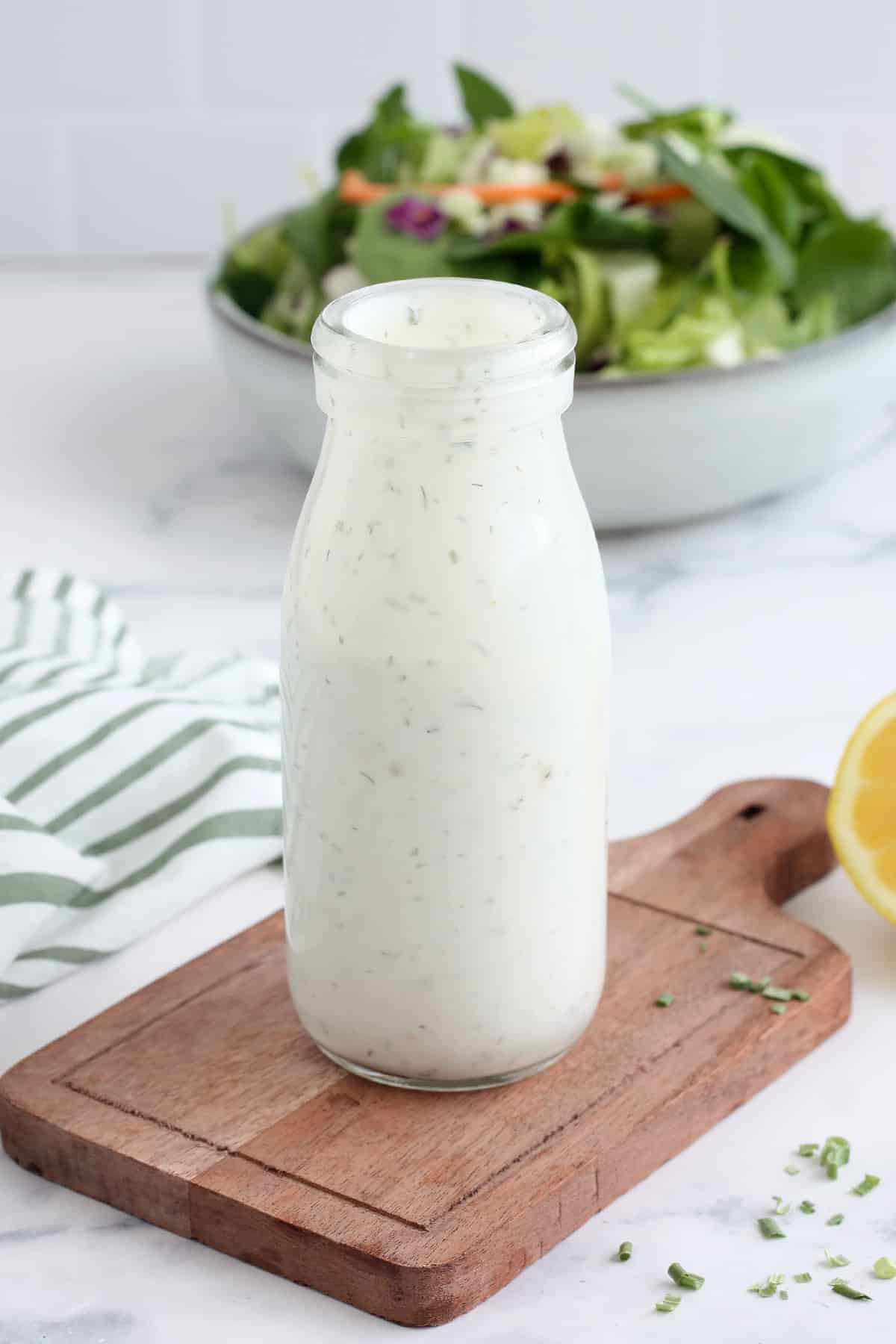 Homemade Ranch Dressing in a glass bottle in front of a large green salad.