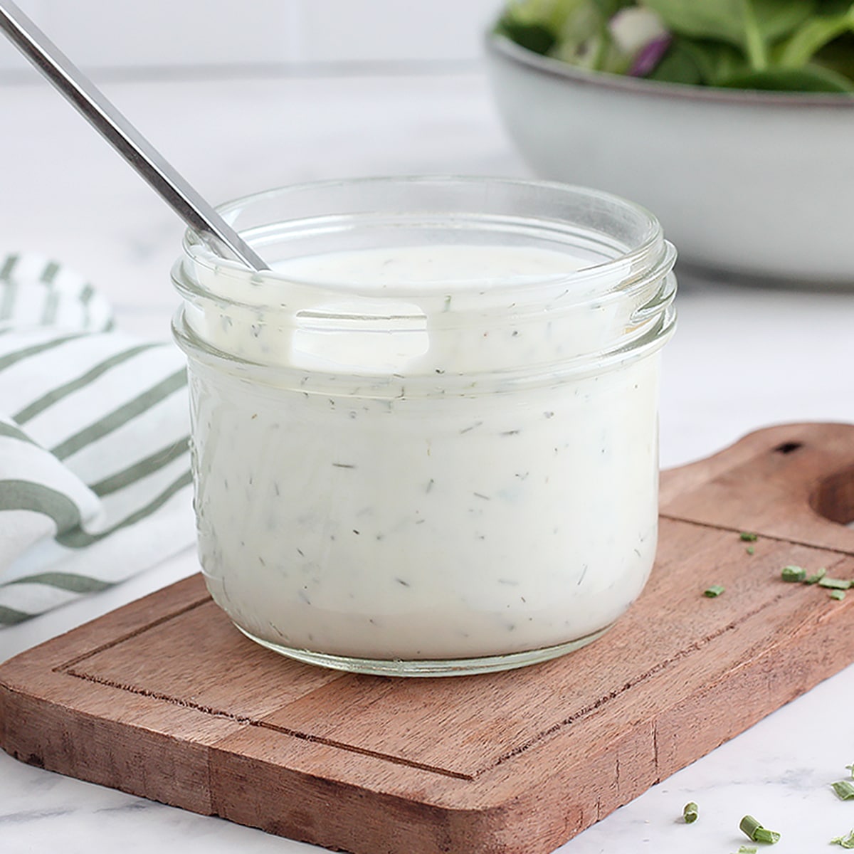 Creamy 5 minute homemade ranch - perfect for a crunchy veggie tray! 6 A small glass jar of ranch dressing with a striped linen and a metal spoon.