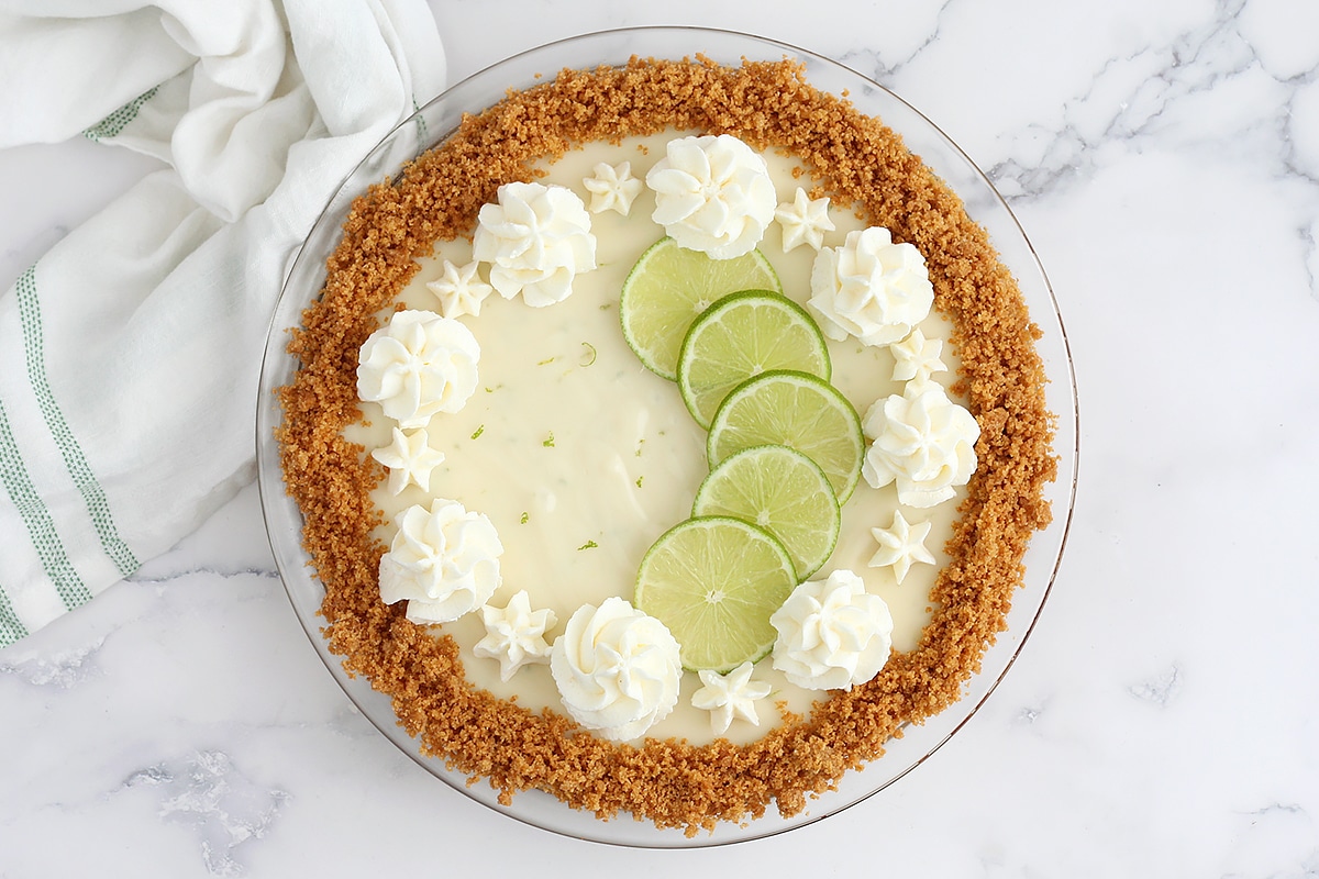 Key lime pie with a graham cracker crust topped with fresh limes and whipped cream.