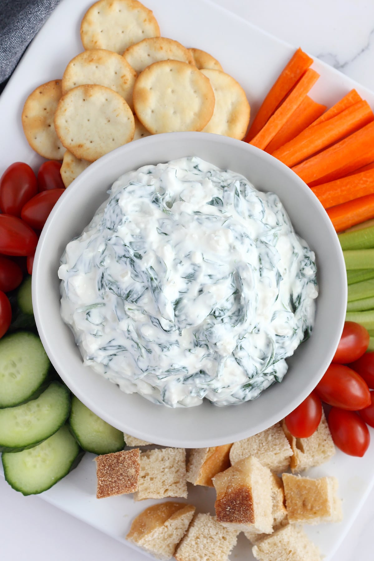 An overhead shot of spinach dip with carrots, celery, cherry tomatoes, crackers, and cucumbers.