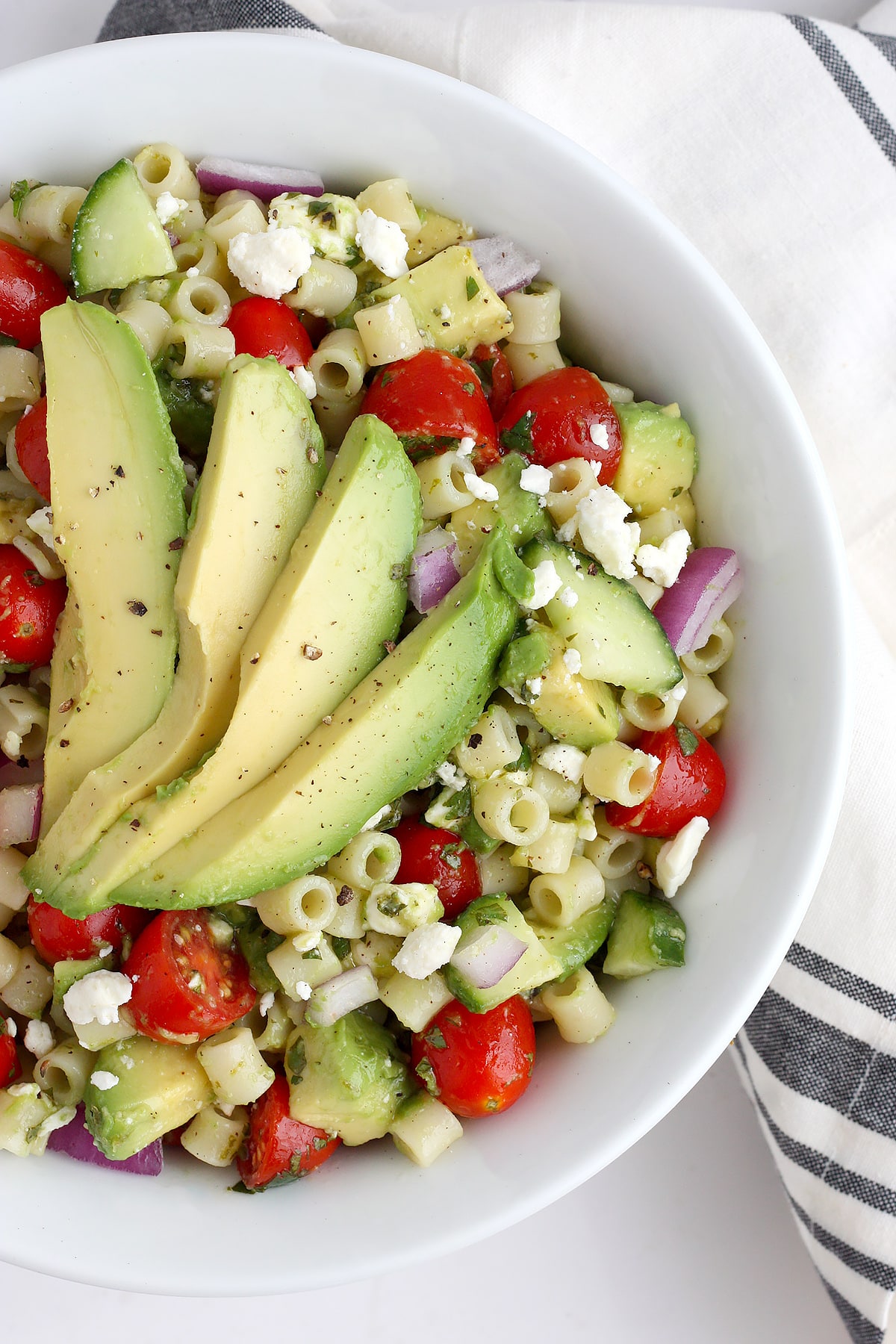 Avocado pasta salad topped with fresh cracked black pepper in a white serving bowl.