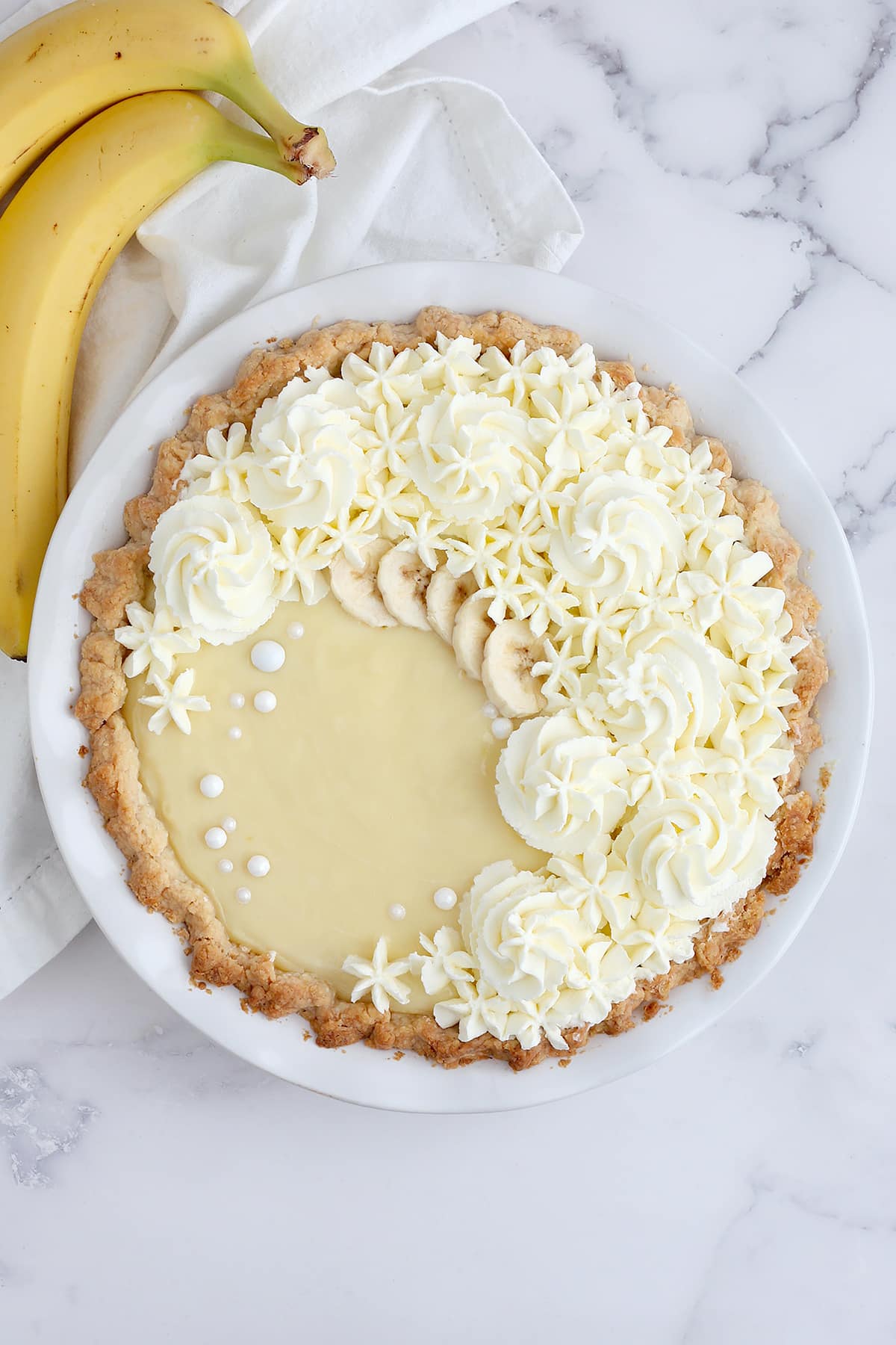 A banana cream pie topped with whipped cream in a white ceramic pie dish.