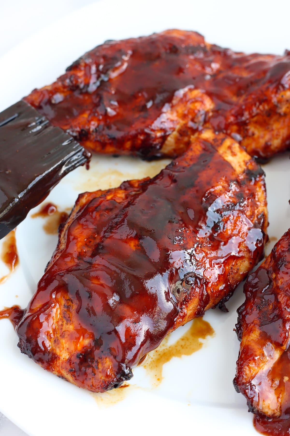 Barbecued chicken breasts coated in bbq sauce on a white plate.