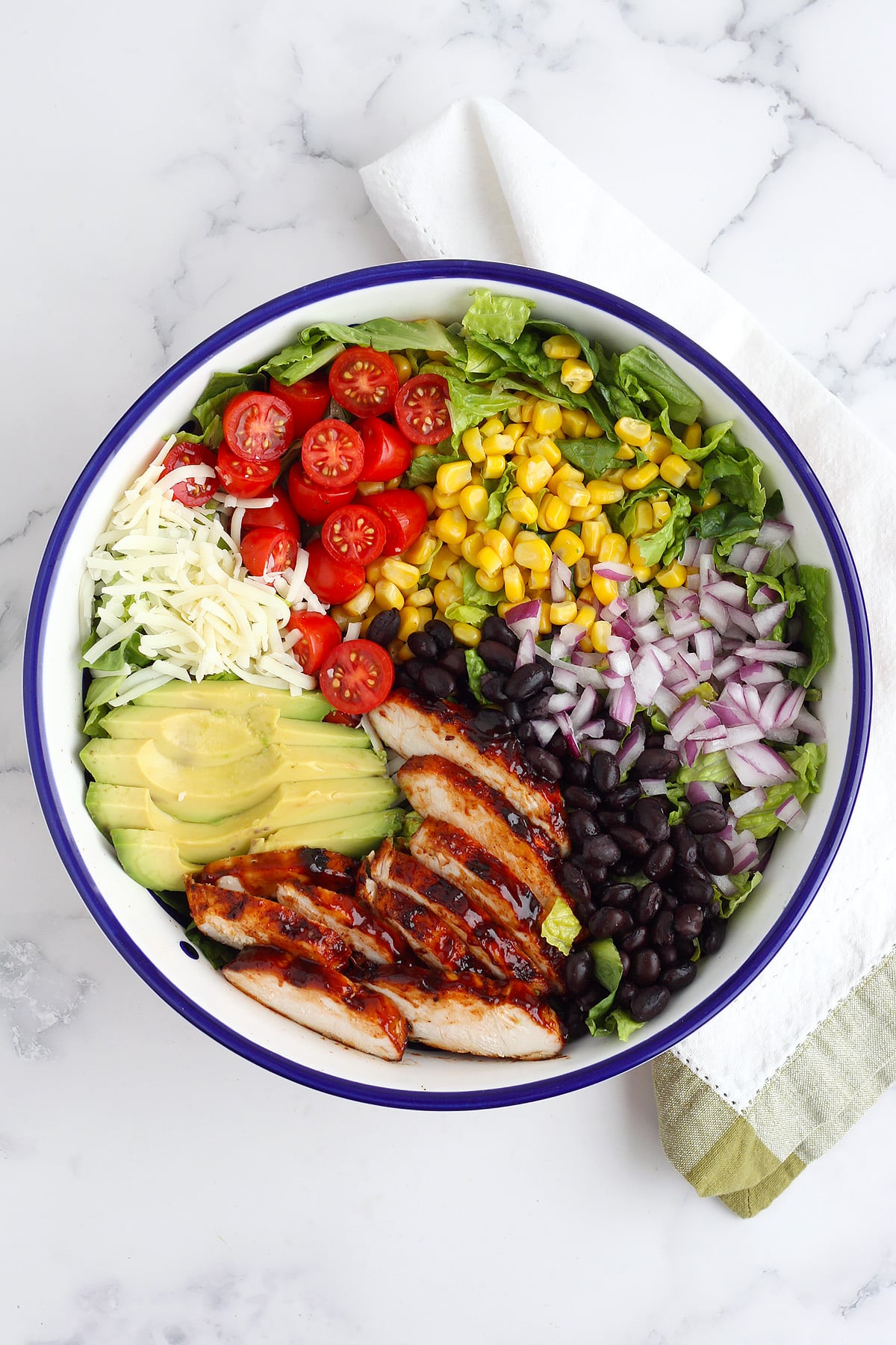 An overhead shot of salad topped with corn, cherry tomatoes, red onion, avocado, and grilled bbq chicken.