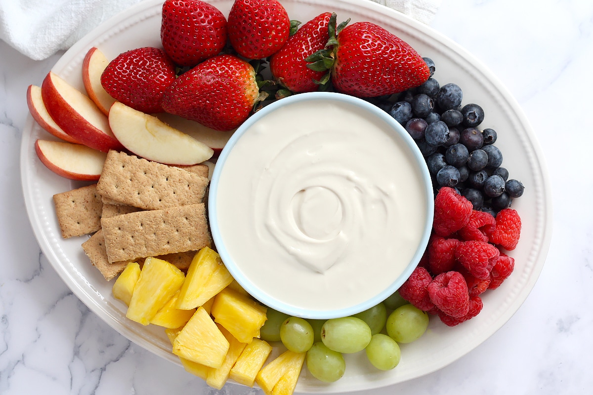 A white, oval platter with assorted fresh fruit and a bowl of fruit dip.
